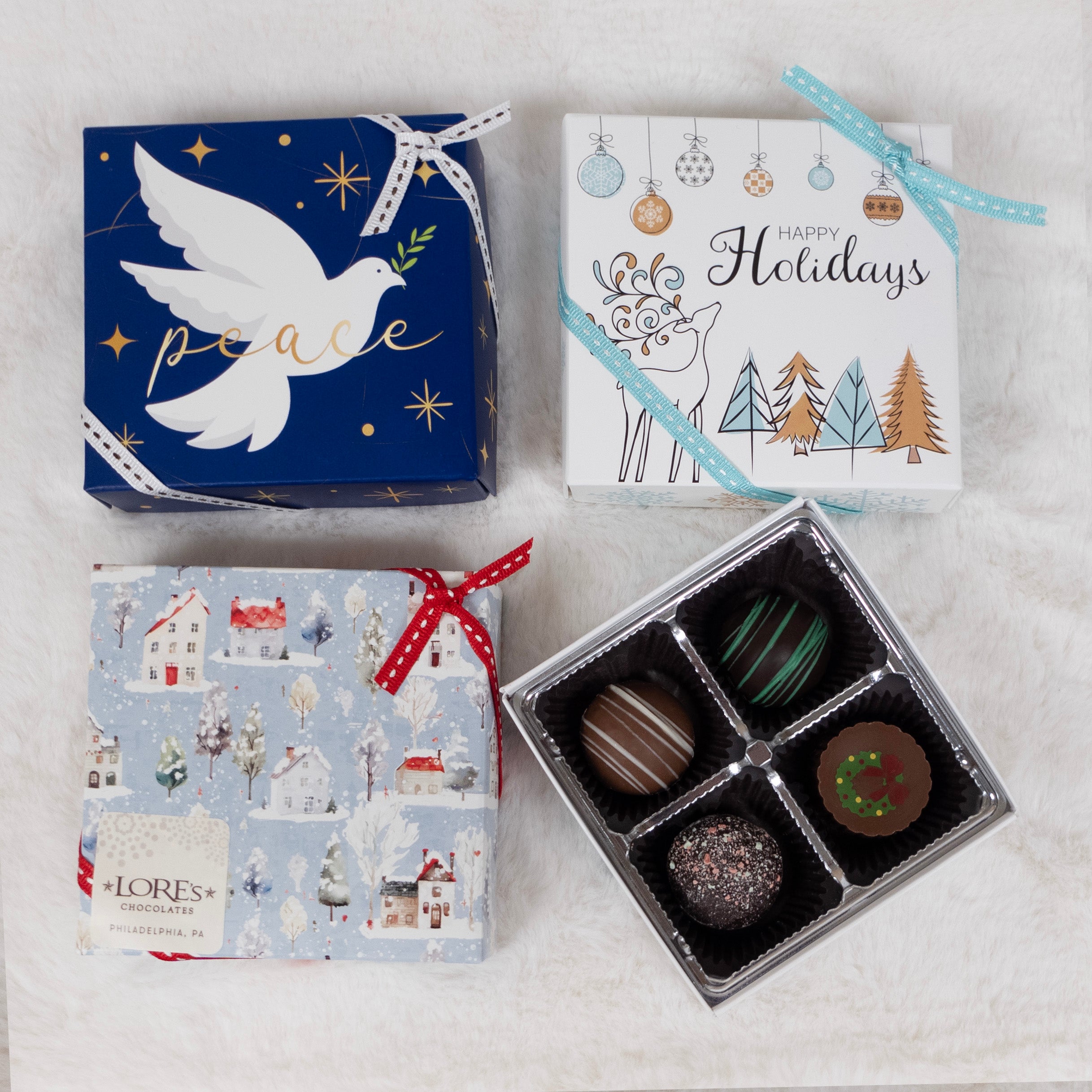 Four Christmas-themed gift boxes with a box of chocolate truffles on a light gray background