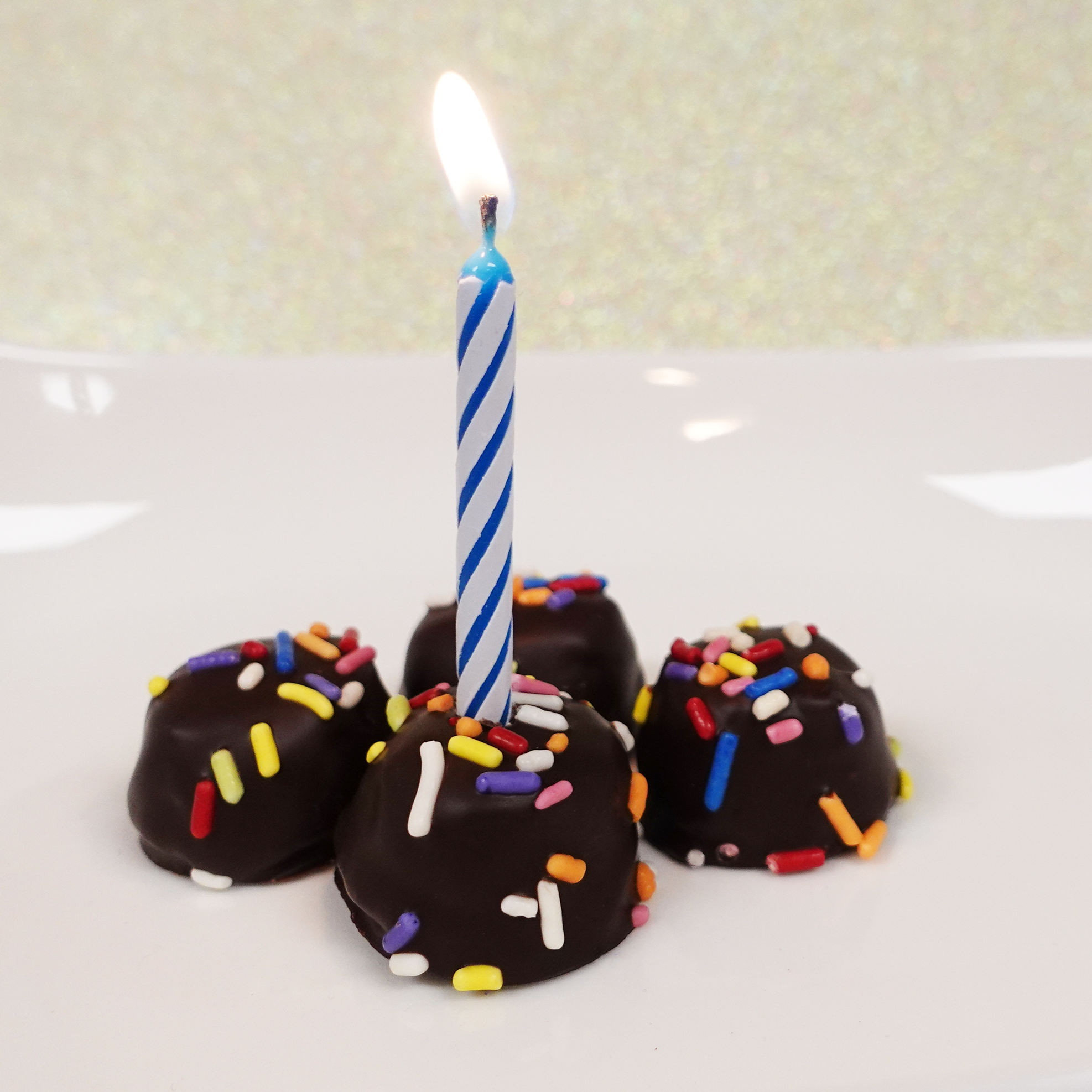 Dark Chocolate birthday cake butter creams with rainbow sprinkles. Image shows a birthday candle in one of the chocolates