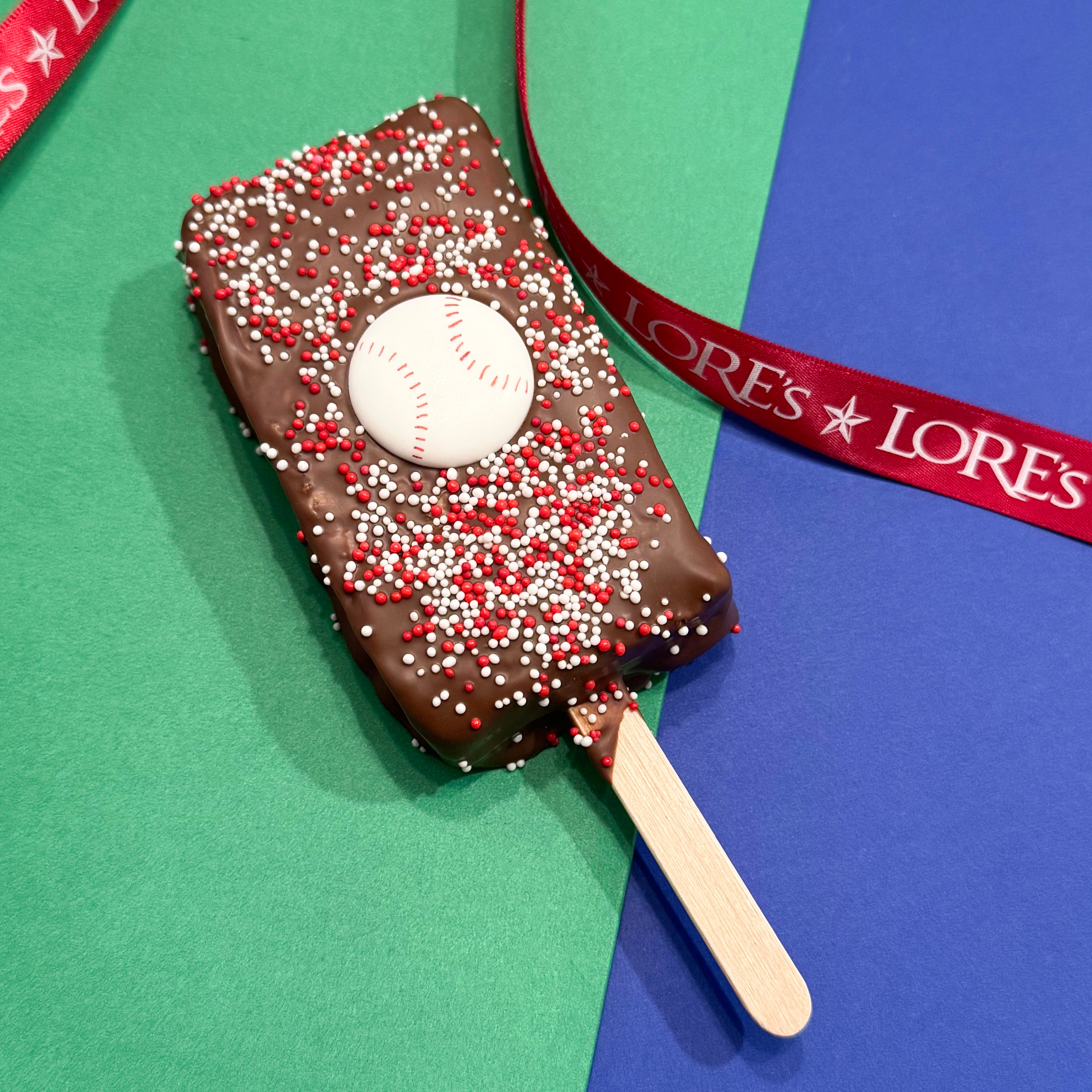 Chocolate-covered Rice Krispies bar with a baseball and Phillie's colors red and white sprinkles, on a green and blue background with 'LORE'S' branding.