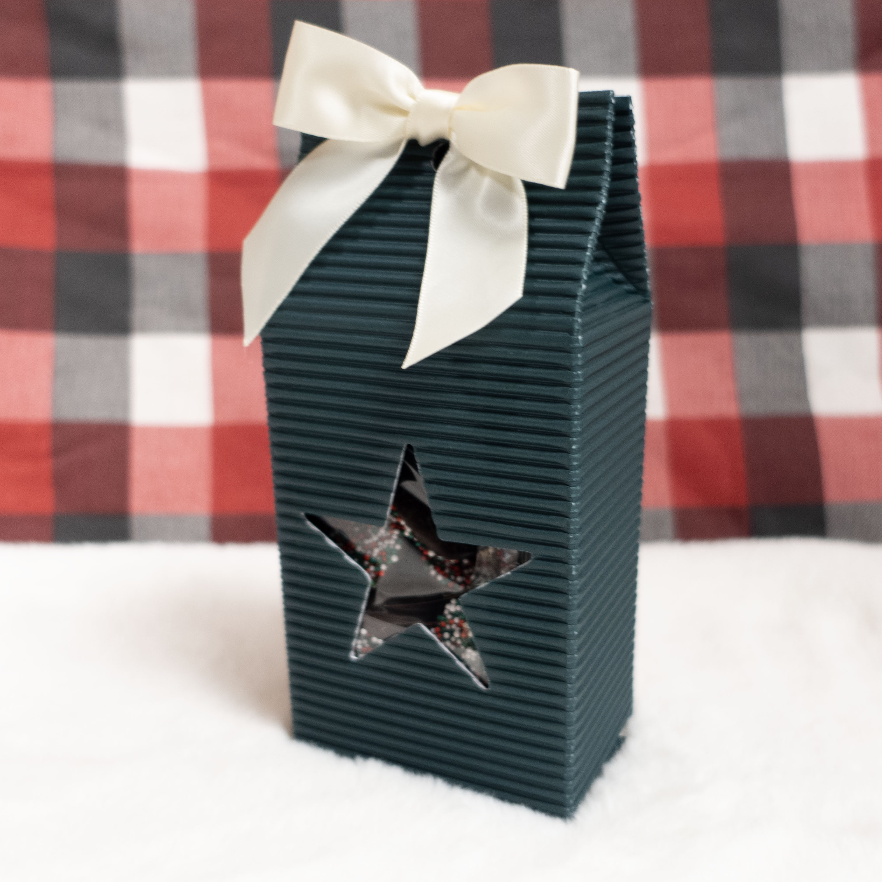 Christmas Nonpareils in Dark green gift box with star cutout and white ribbon against a red and black checkered background