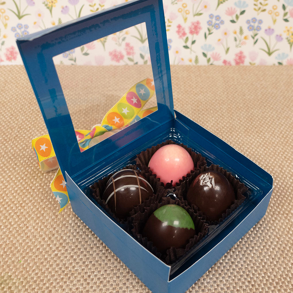 Open blue box containing assorted large chocolate truffles on a floral-patterned surface