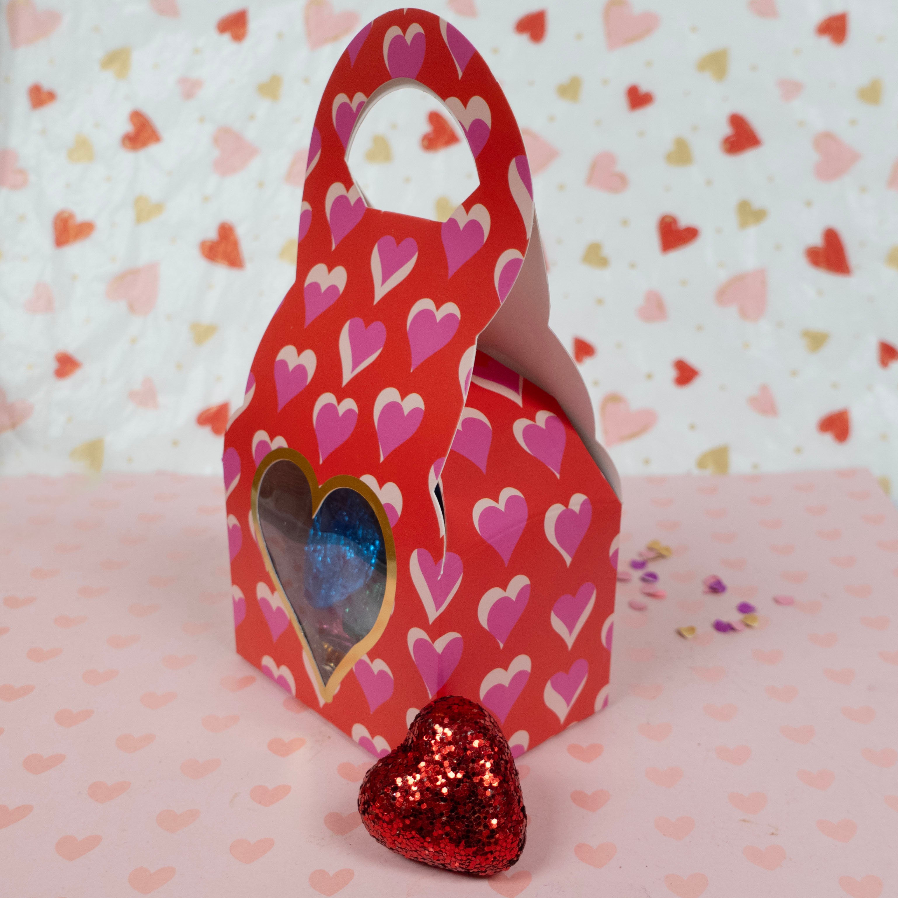 Red gift box with heart pattern and filled with foiled milk chocolate hearts on a heart-patterned background