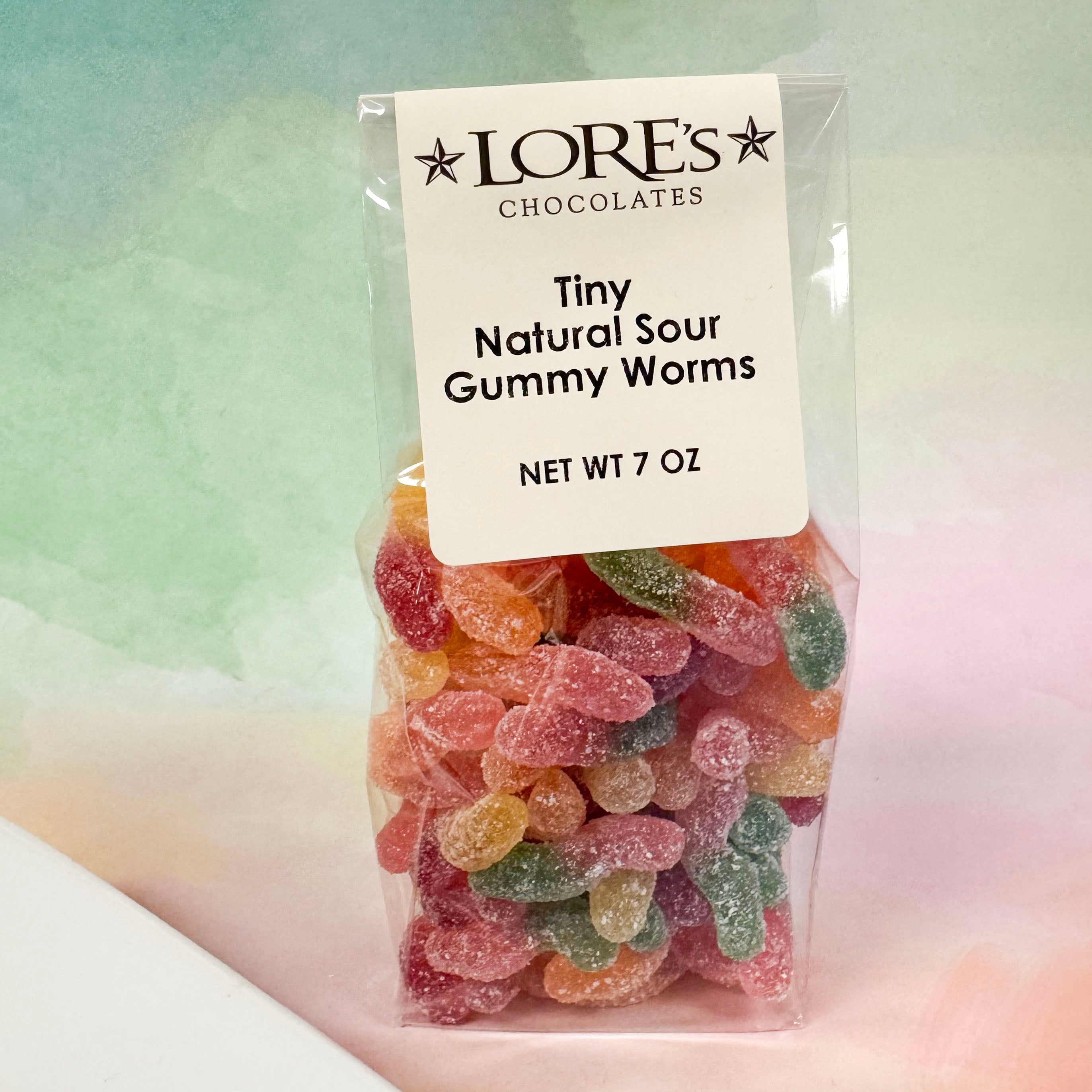 Packaged Tiny Natural Sour Gummy Worms from Lore's Chocolates with a label on a gradient background.