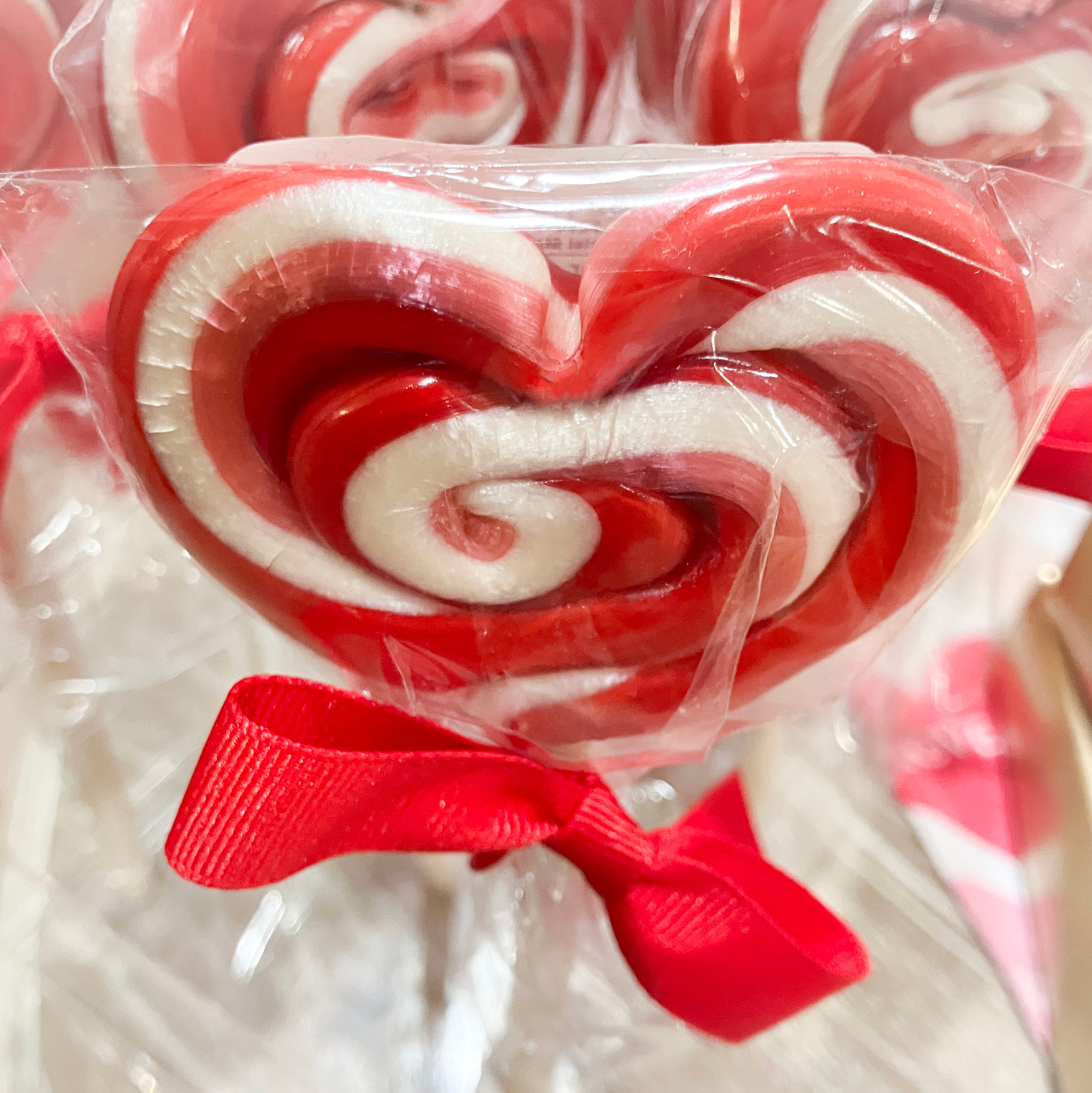 Red and white heart-shaped swirl lollipops with a red bow in clear packaging.