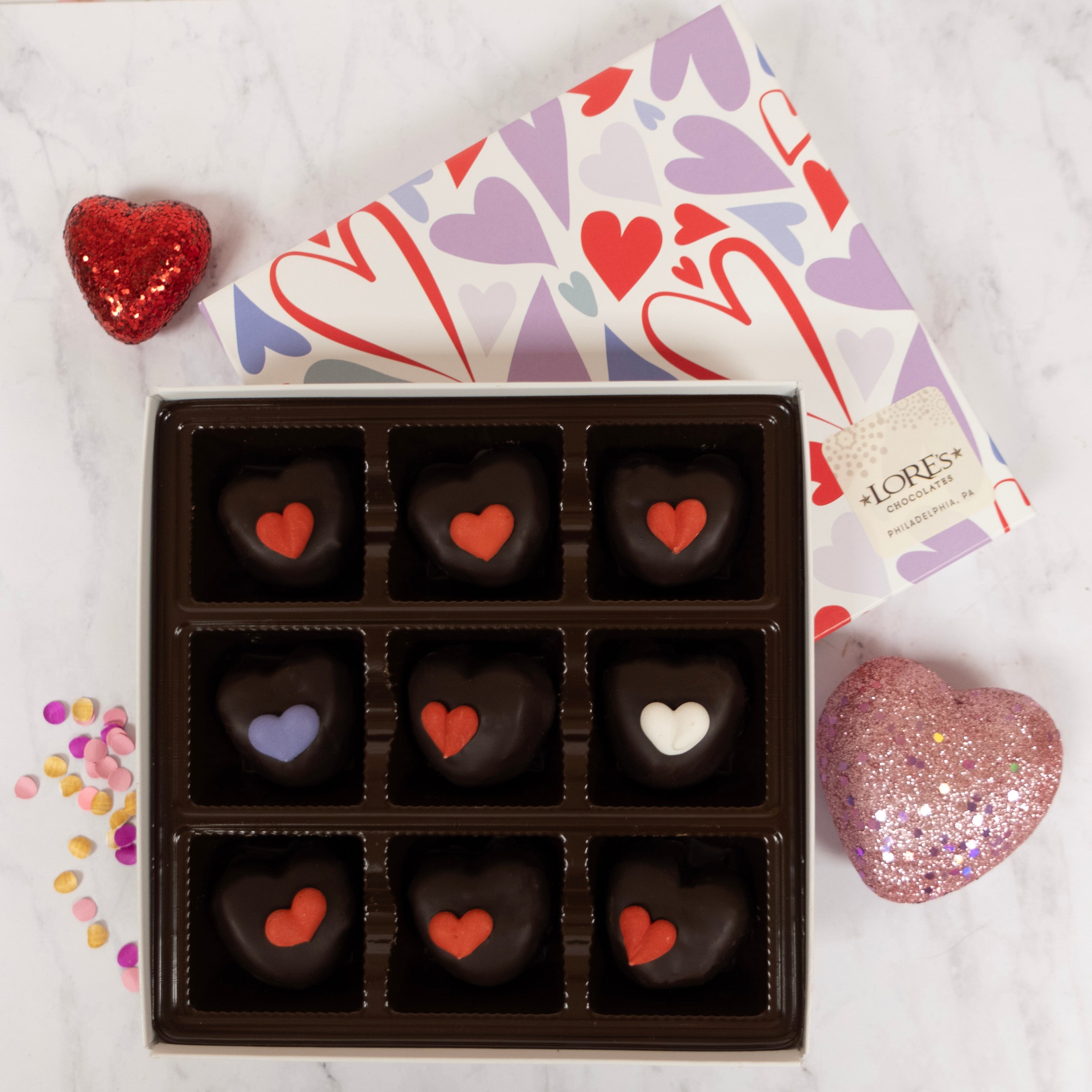Box of heart-shaped dark chocolates with colorful hearts on a white background