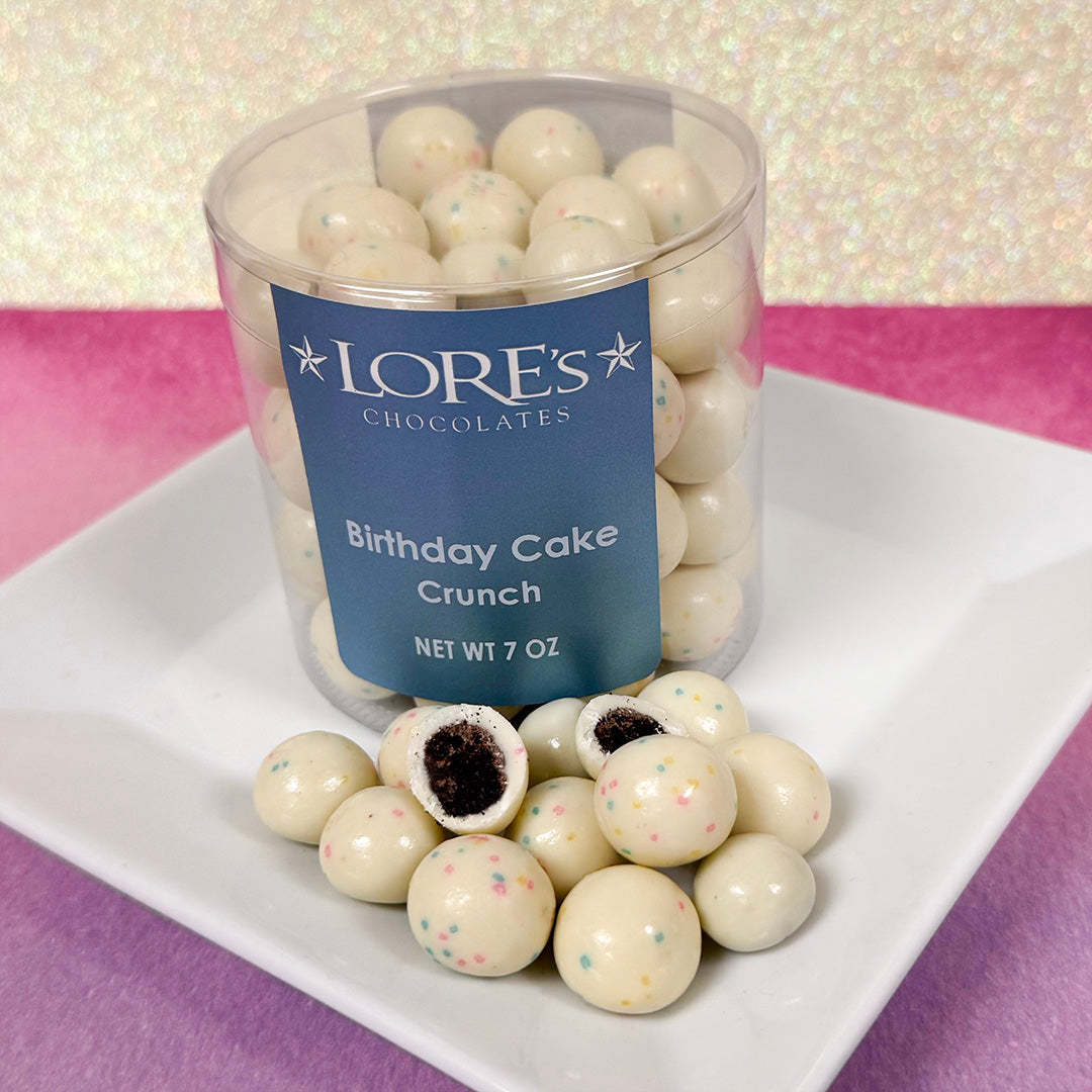 Clear container of Lore's Chocolates Birthday Cake Crunch on a white plate with a pink background - sold in Philadelphia