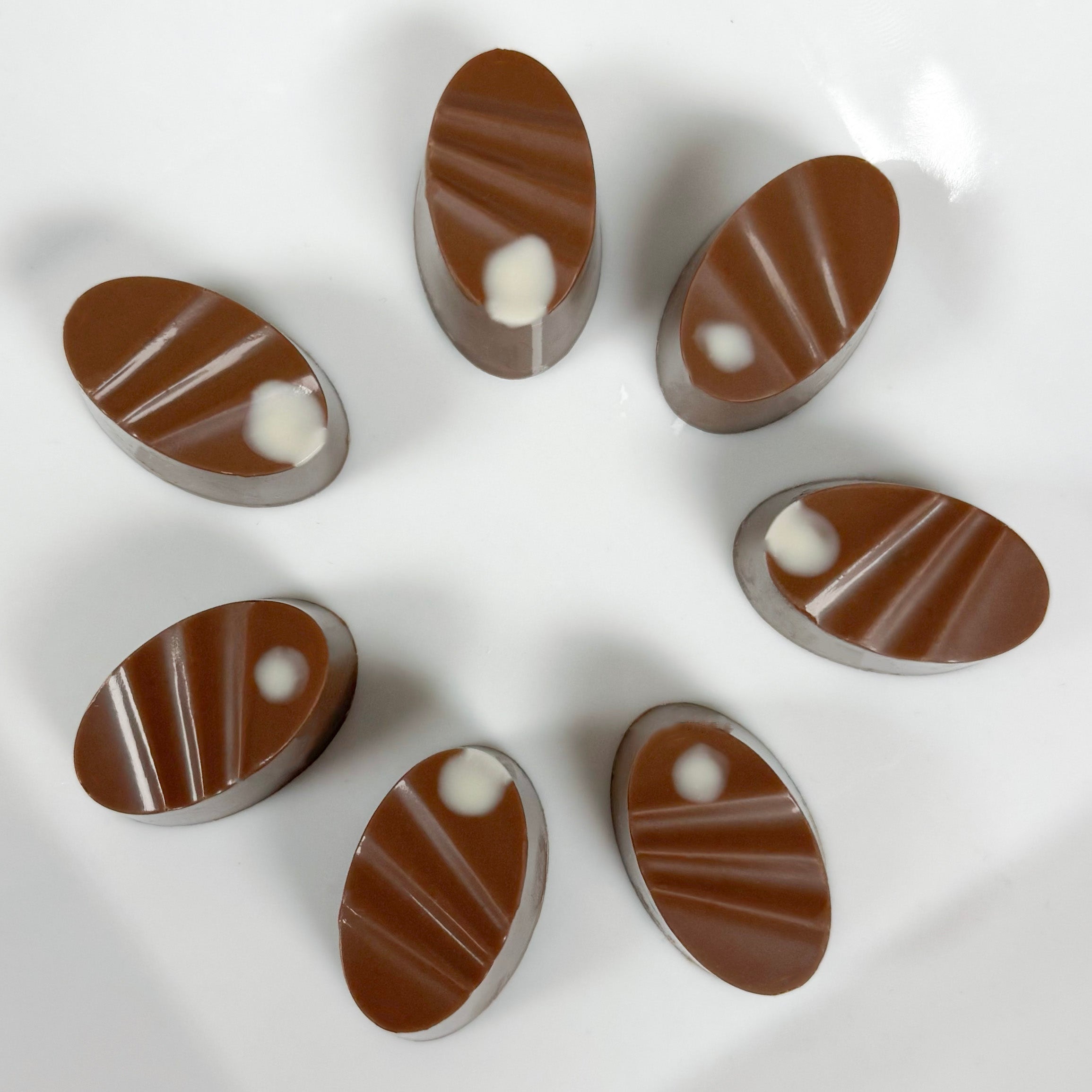 Six oval-shaped milk chocolate pieces with a white dot, arranged in a circle on a white background.
