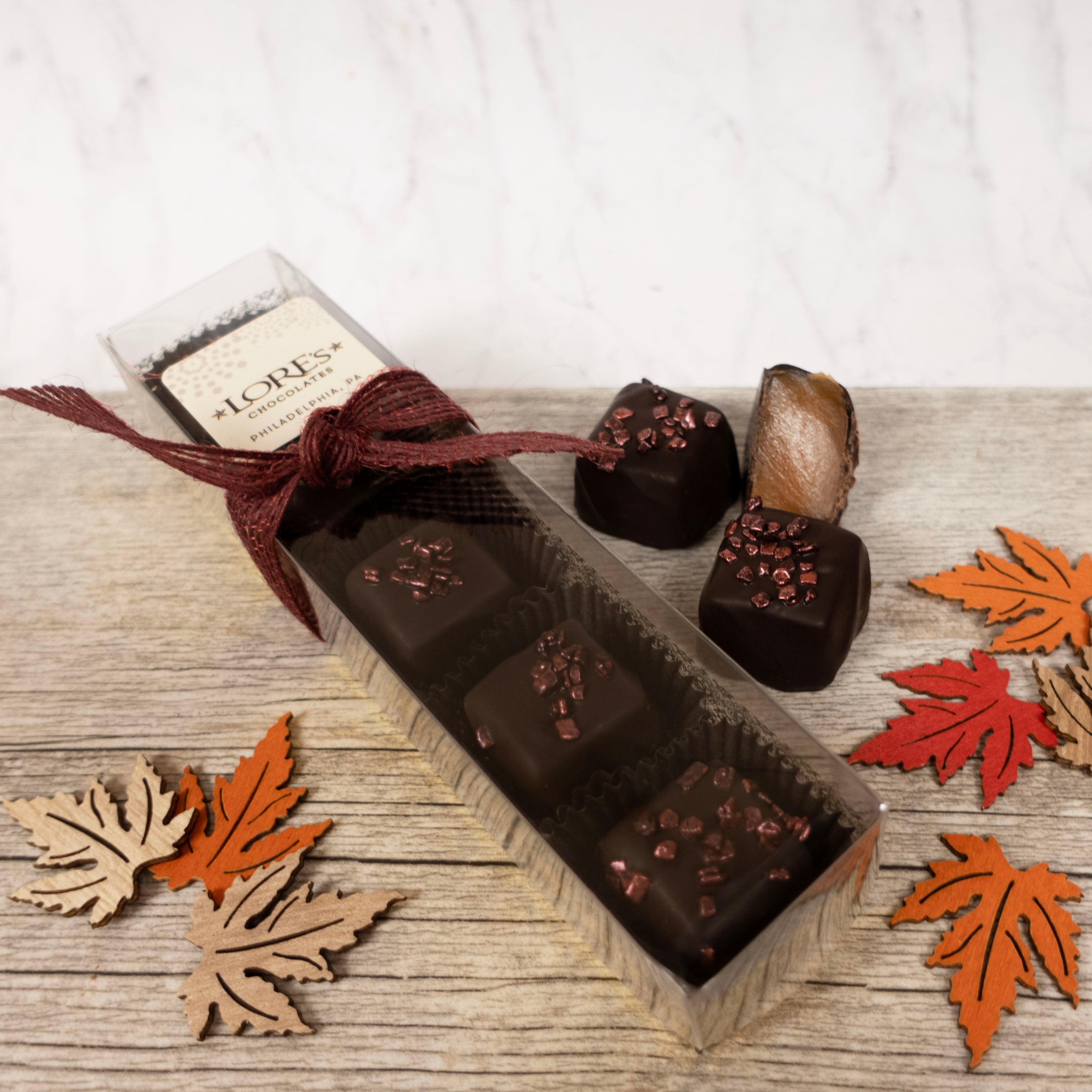 Dark Chocolate caramels in a box with decorative leaves on a wooden surface