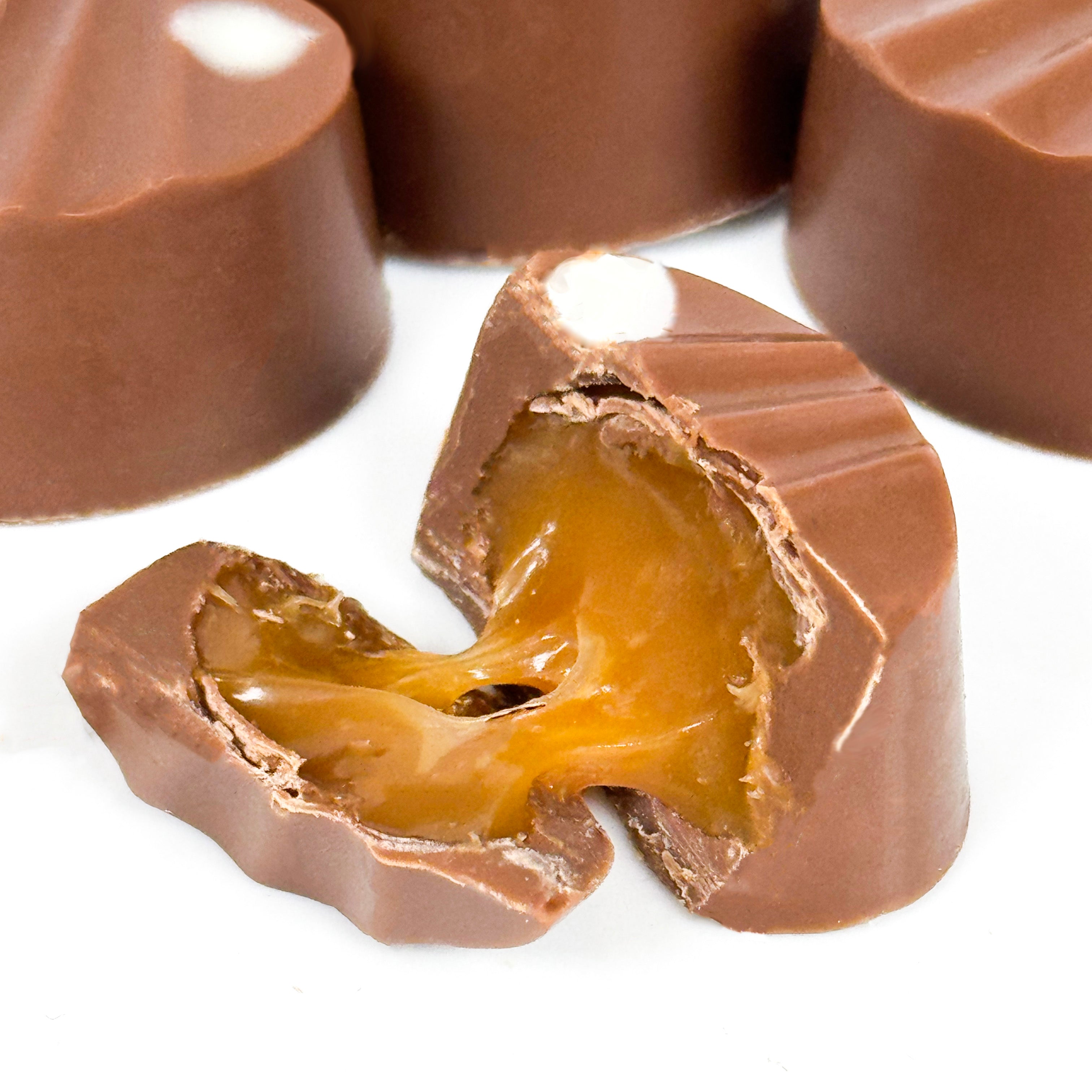 A close-up of milk-chocolate-covered caramel candies, with one cut in half to show the rich caramel filling stretching out against a white background.