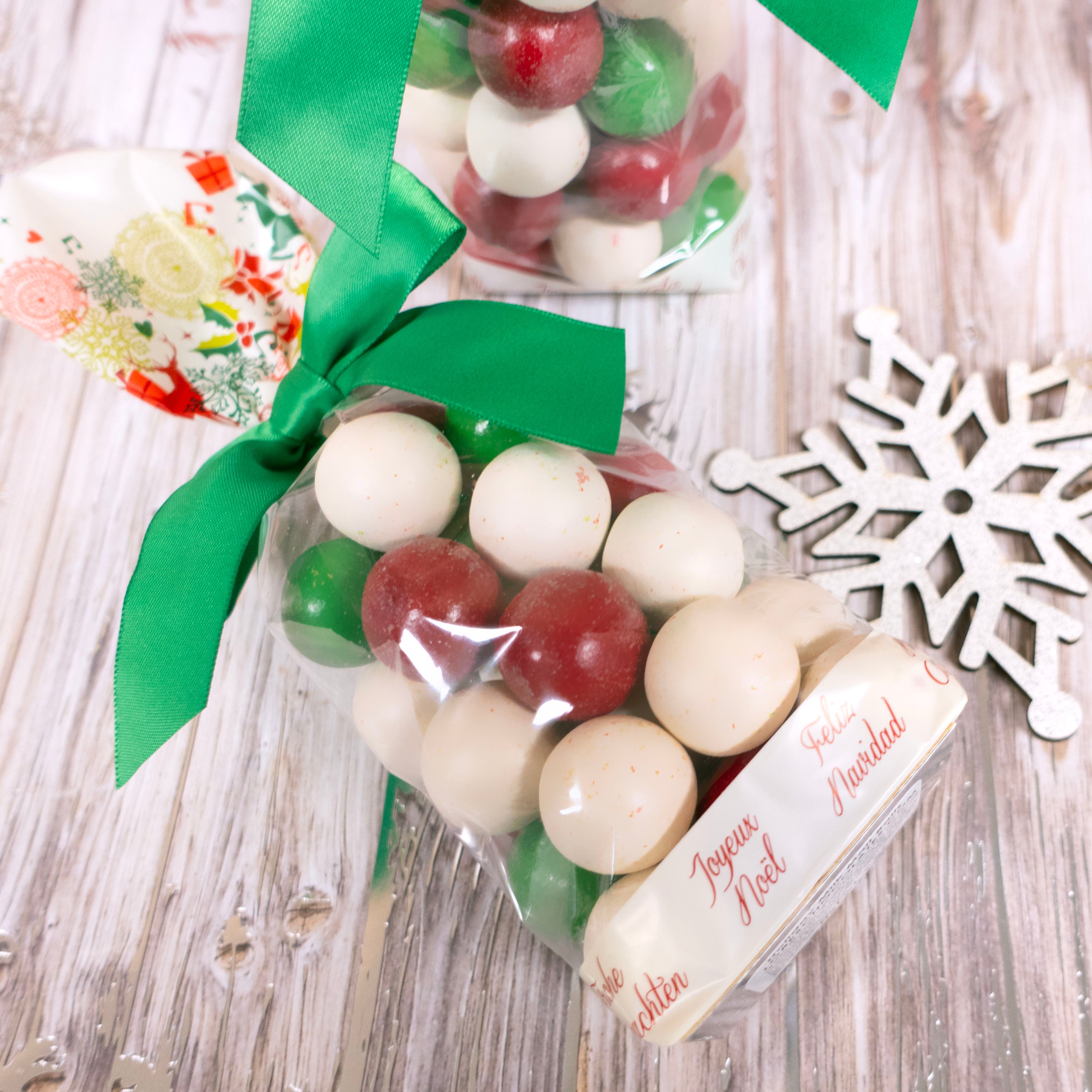 Packaged assorted red, white, and green milk chocolate malt balls with a green ribbon on a wooden surface.