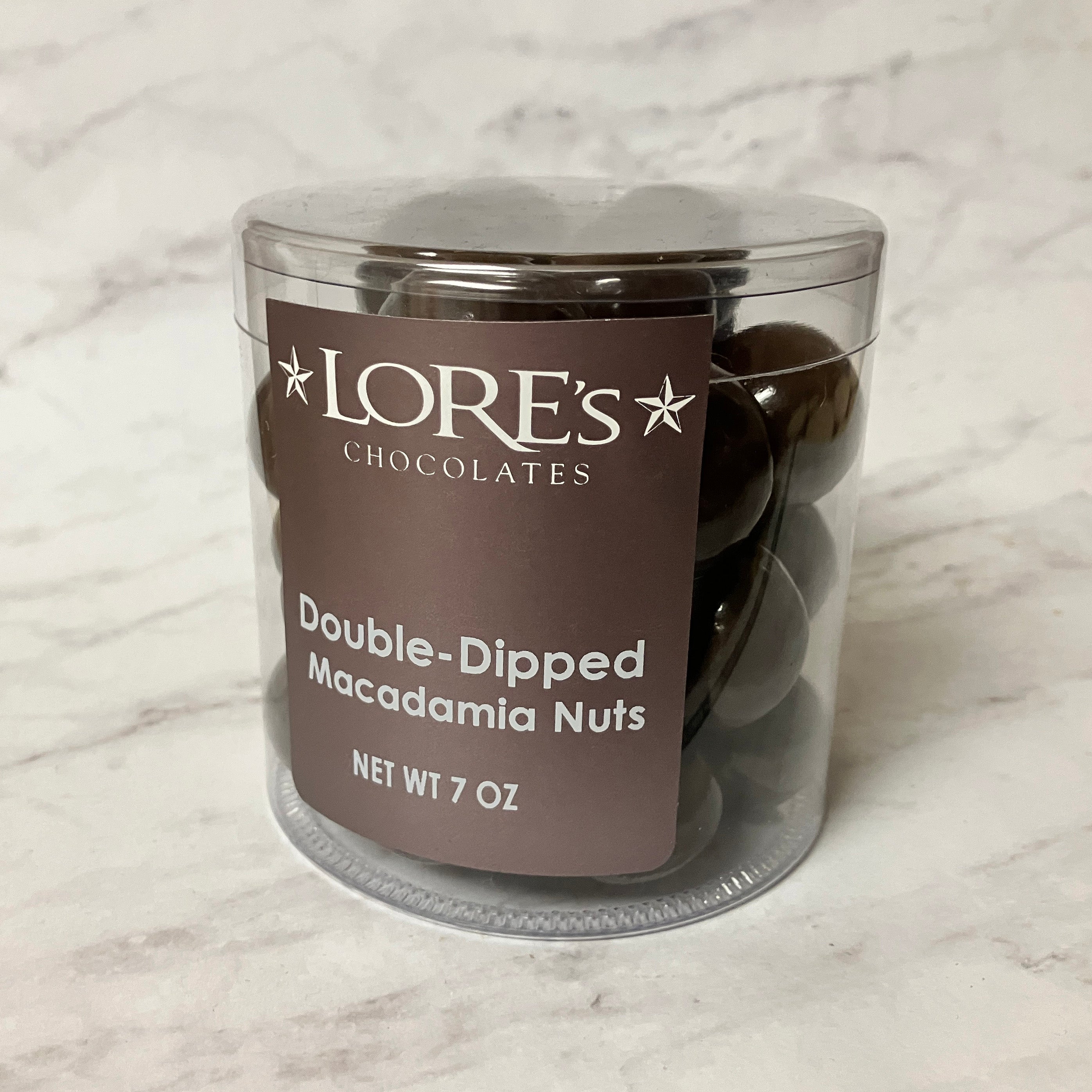 Container of Lore's Chocolates Double-Dipped Macadamia Nuts on a marble surface