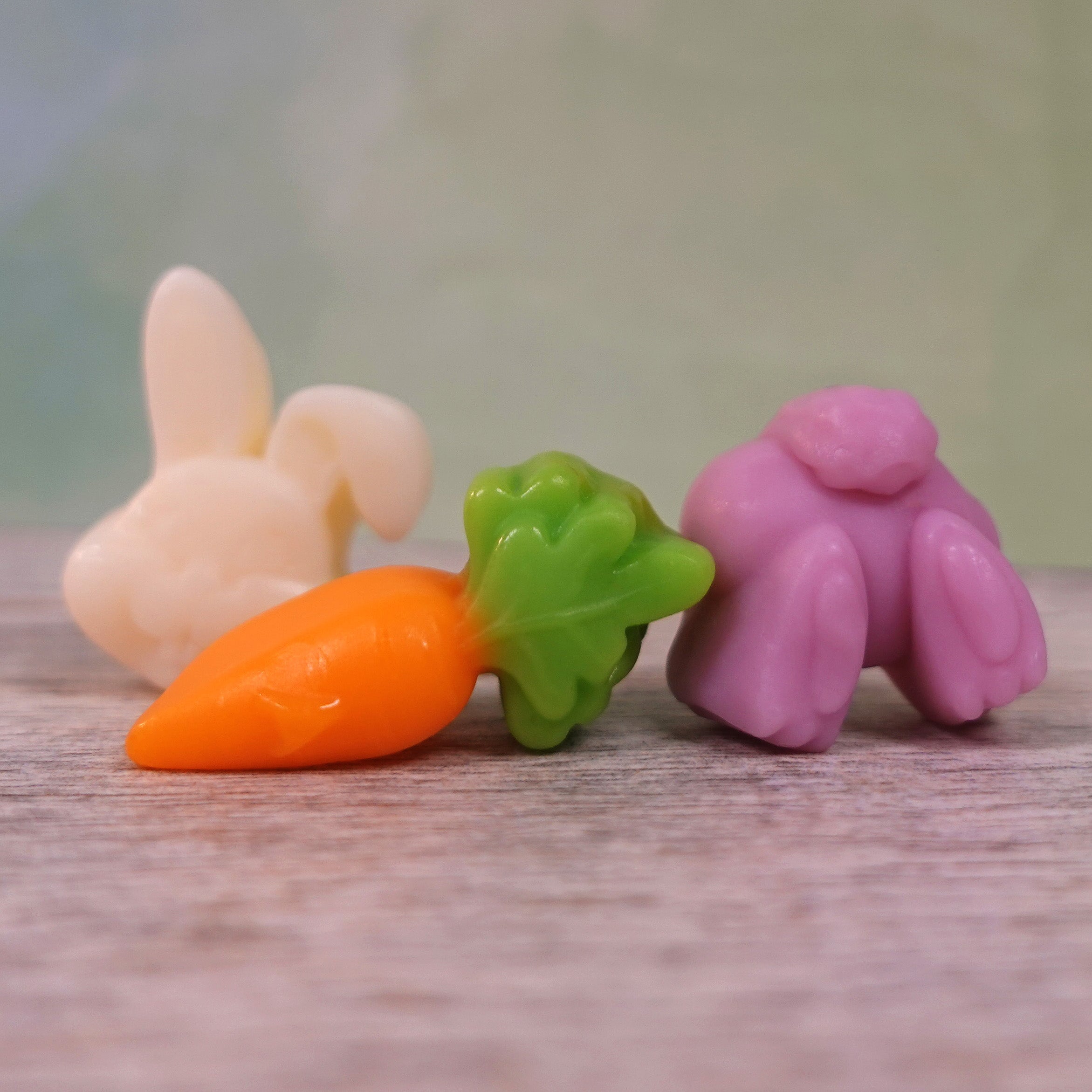 Three colorful gummy candies shaped like a rabbit, carrot, and bunny tail on a wooden surface.