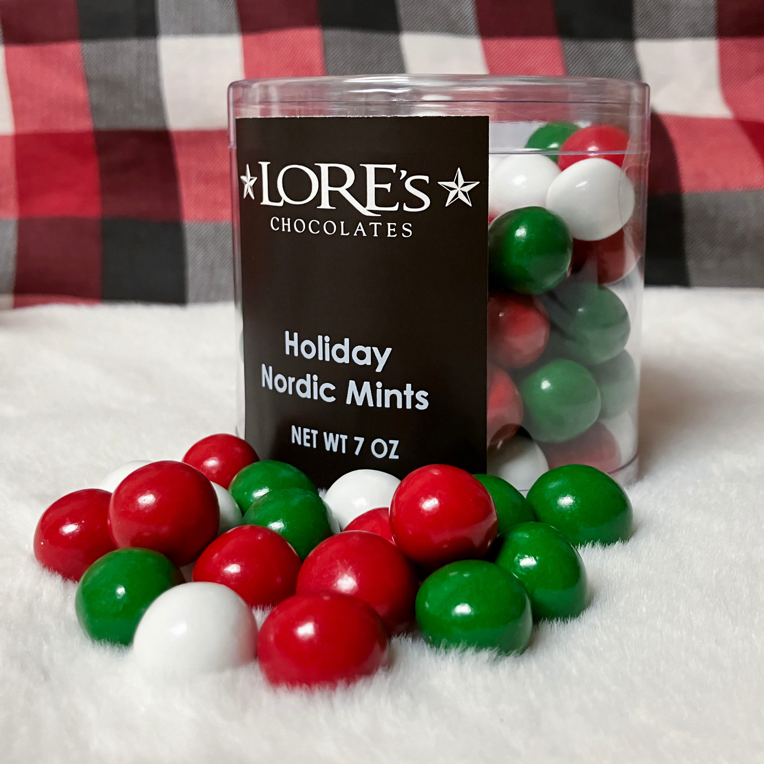 Container of LORE'S CHOCOLATES Holiday Nordic Mints with red, green, and white mints on a checkered fabric background.