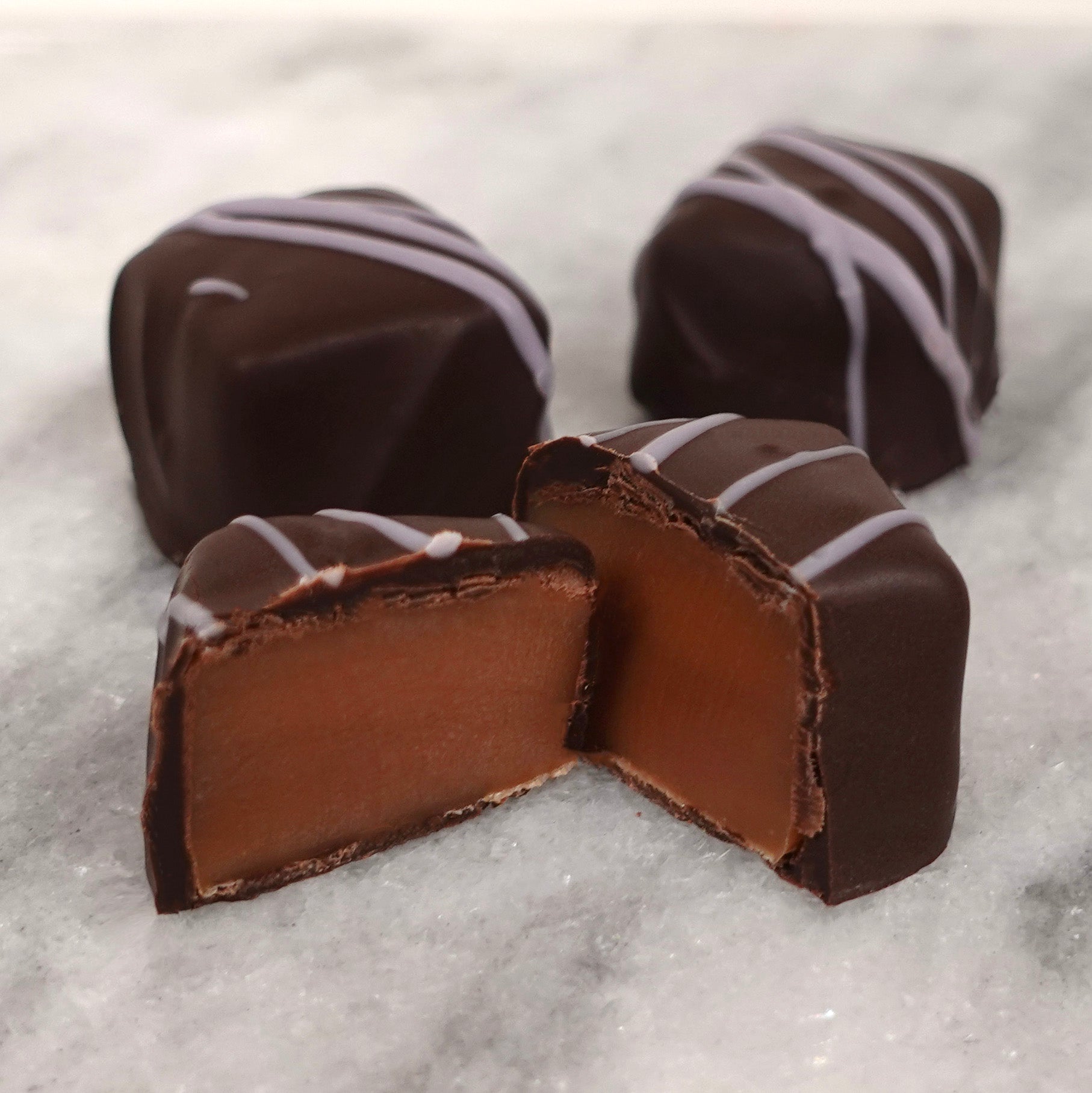 Chocolate caramels, light purple stringing on top, with a couple cut open on a white background