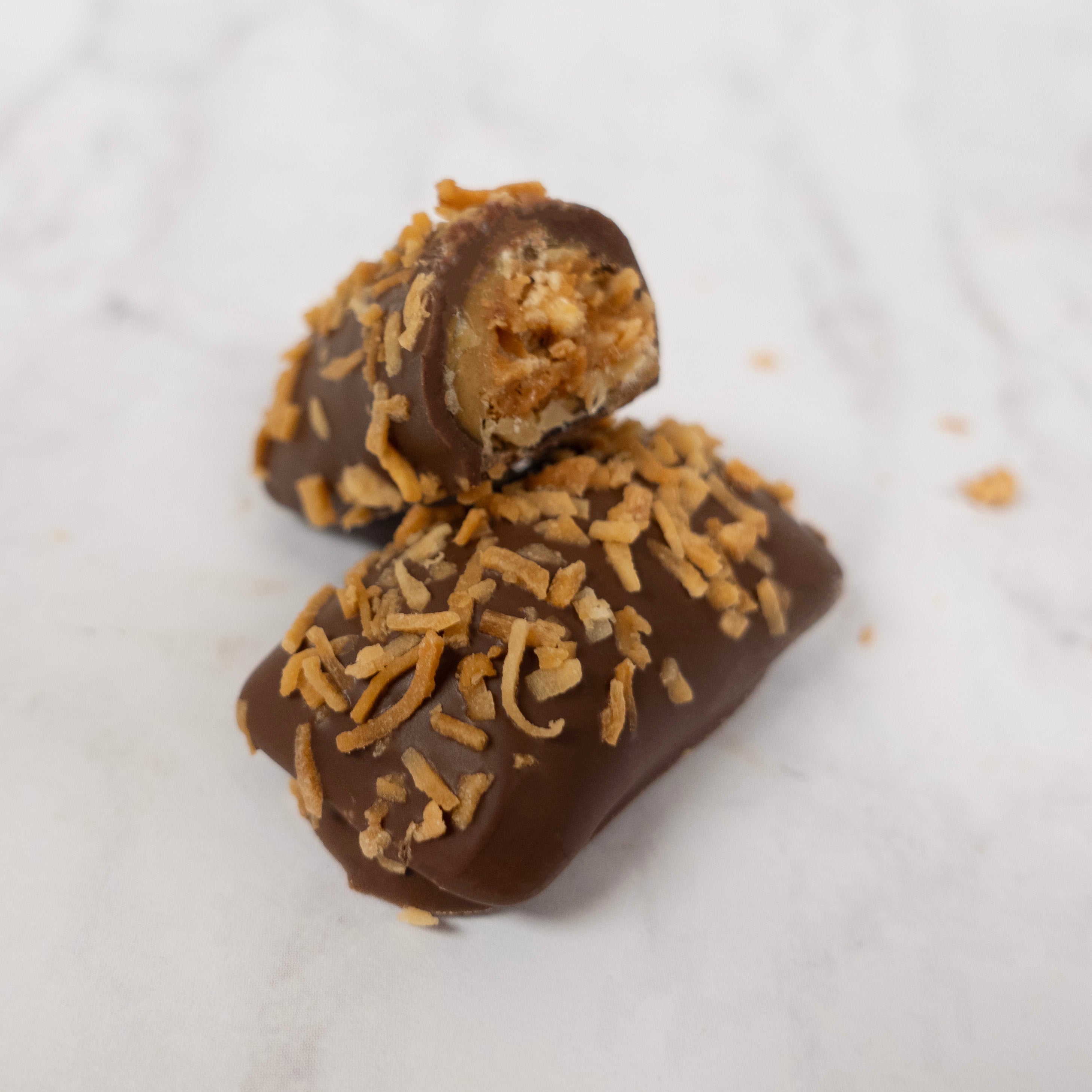 Close up of a milk chocolate covered peanut butter candy with toasted coconut flakes on top