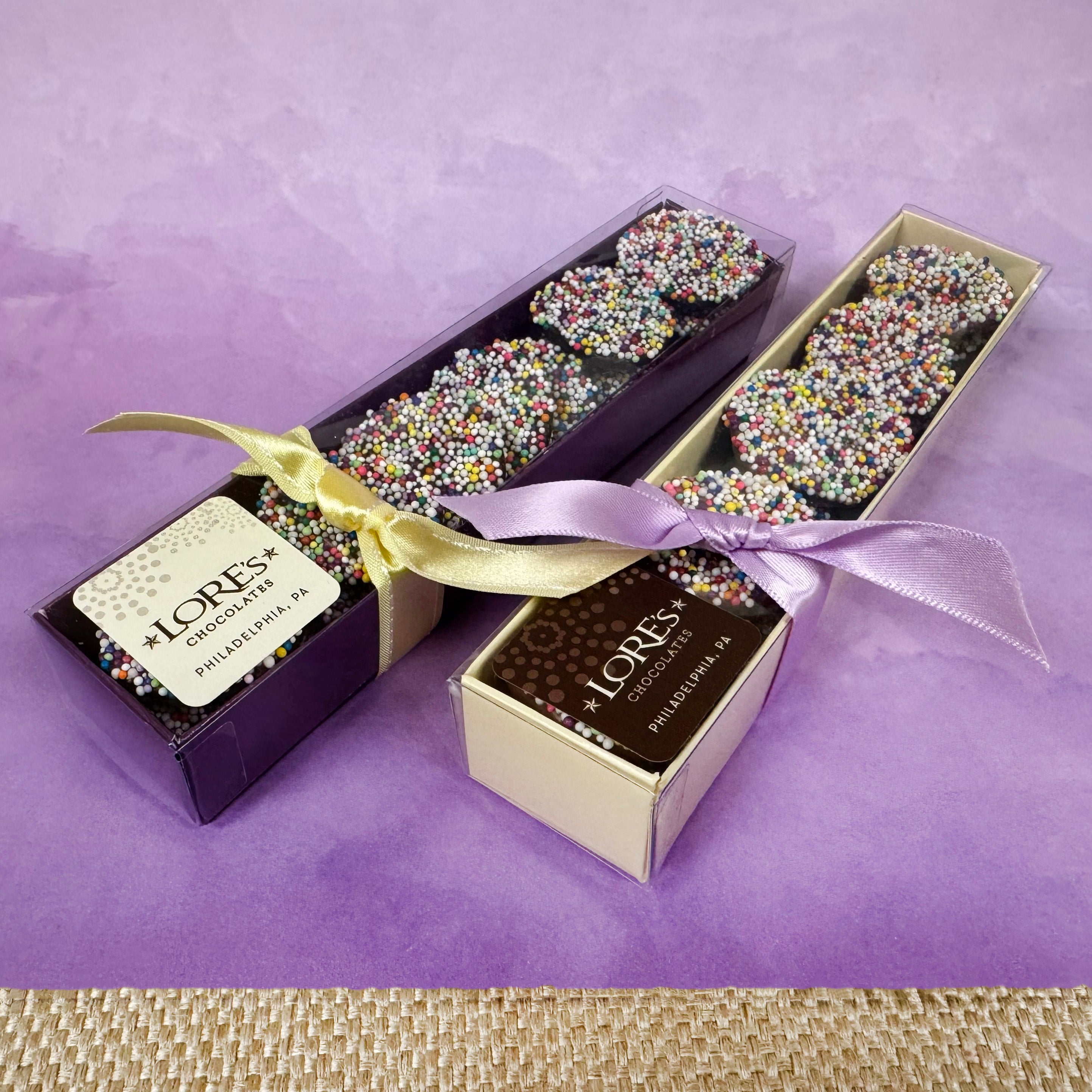 Two boxes of Lore's Chocolates nonpareils on a purple background