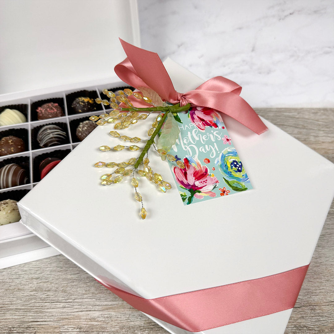 Gift box with truffle chocolates, pink ribbon, and 'Happy Mother's Day' tag on a wooden surface.