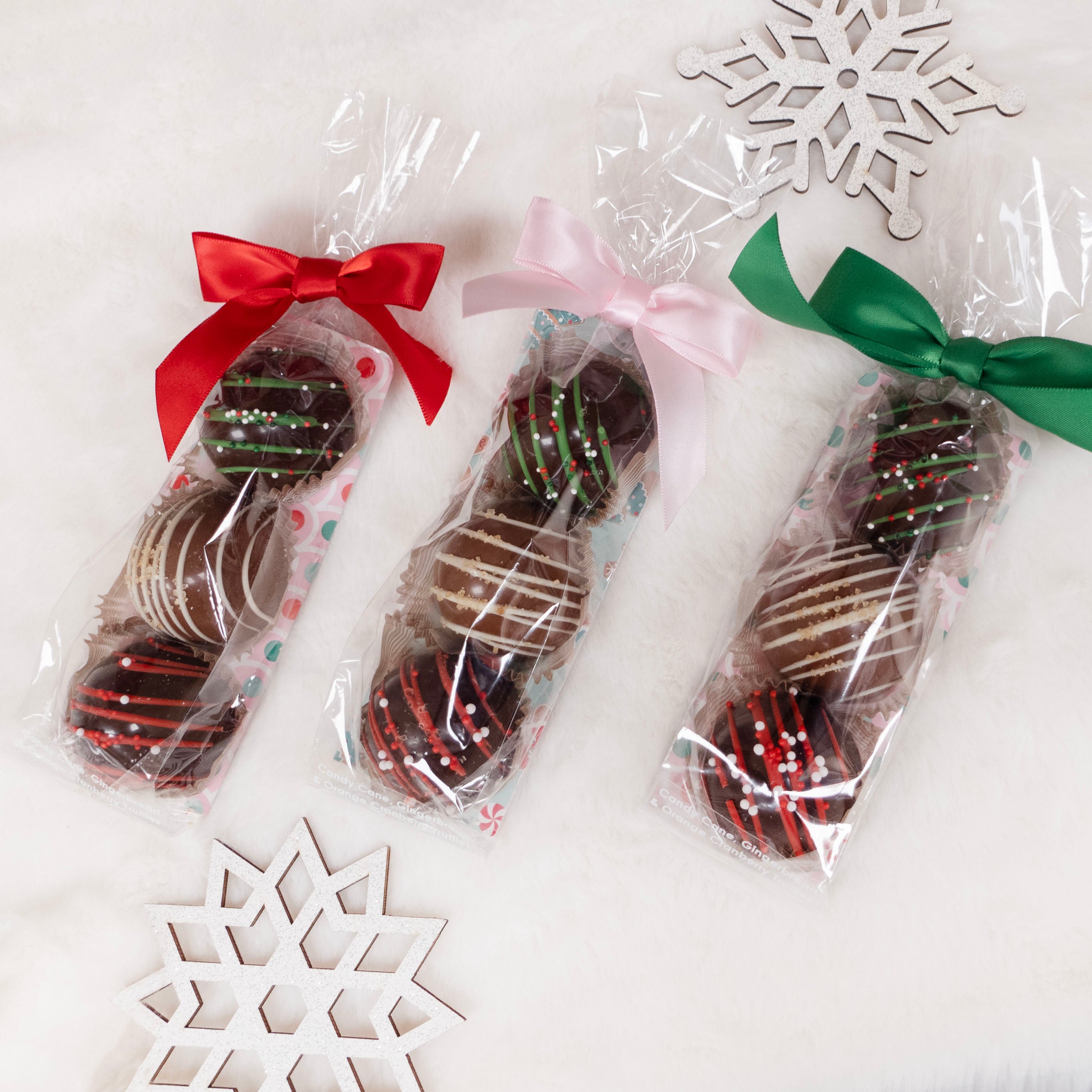 Large Chocolate truffles in clear packaging with red, pink, and green ribbons on a white background.