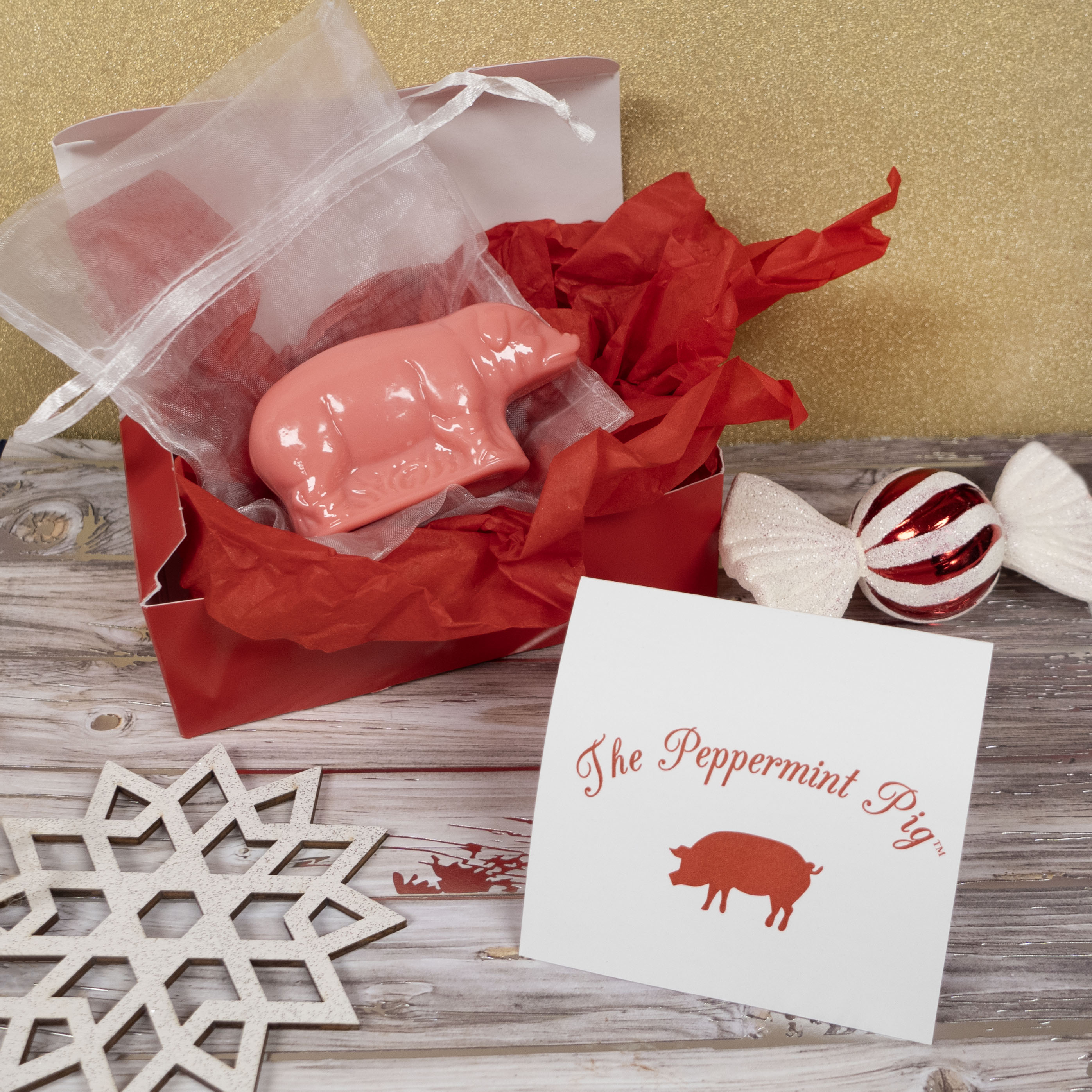 Pink pig-shaped candy in red tissue paper with a card labeled 'The Peppermint Pig' on a wooden surface.