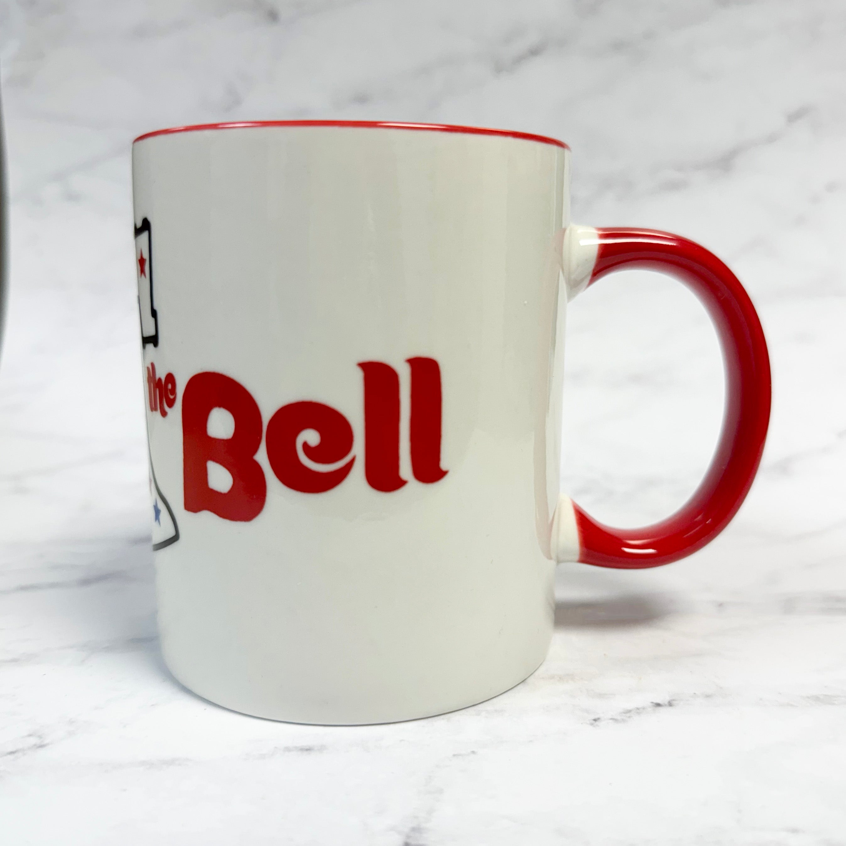 White mug with red interior and handle, featuring text and a logo on a white background - ring the bell philly
