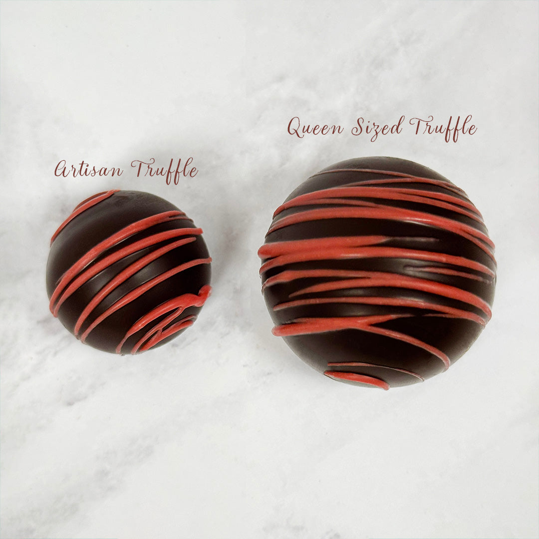 Two strawberry dark chocolate truffles with red drizzle on a white marble surface, labeled 'Artisan Truffle' and 'Queen Sized Truffle'. Sold at Lore's Chocolates in Philadelphia