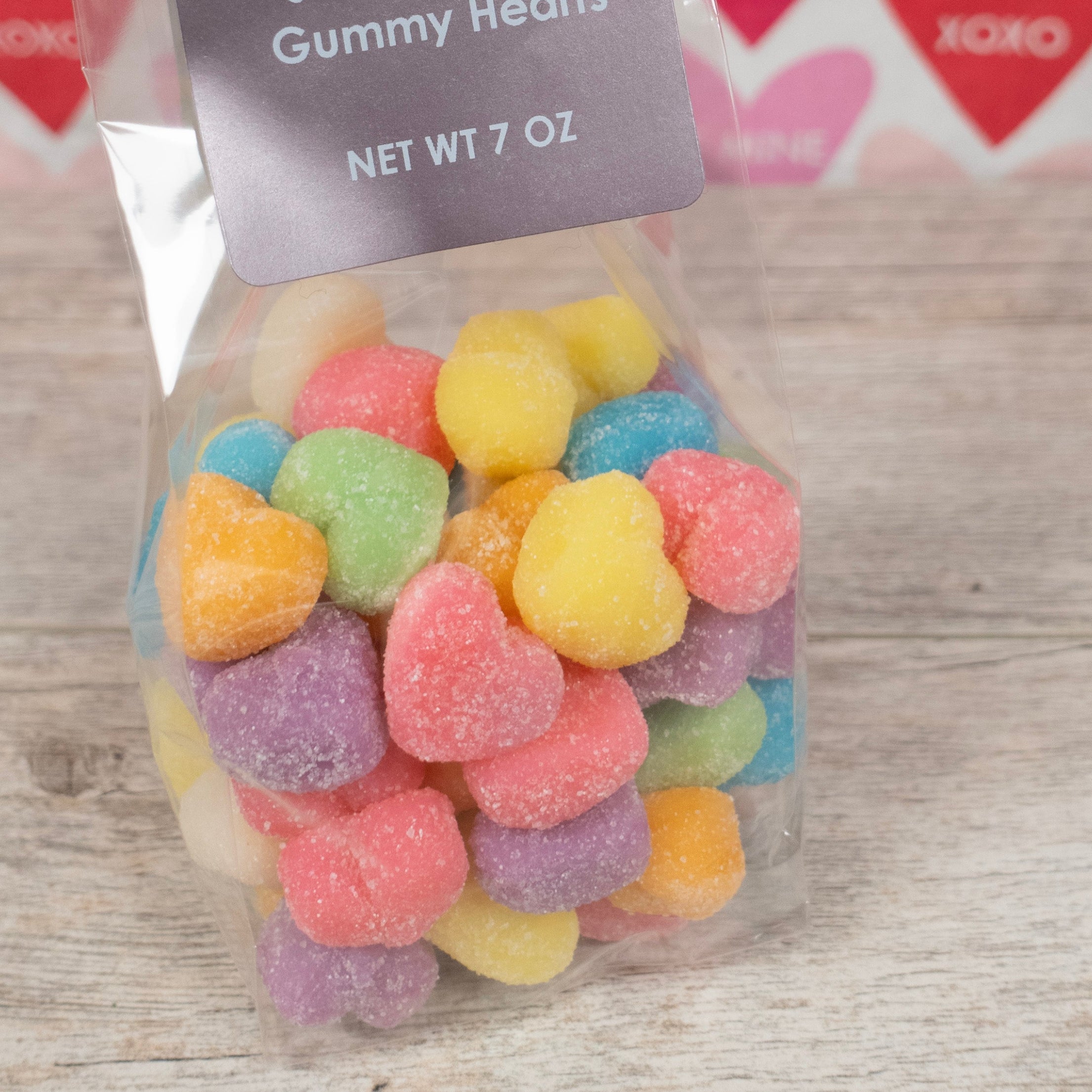 rainbow colored gummies in the shape of hearts for valentine's day pink, green, orange, purple, blue, yellow- label reads "Lore's Chocolates, Share the Love Gummy Hearts Net Wt 7 oz"
