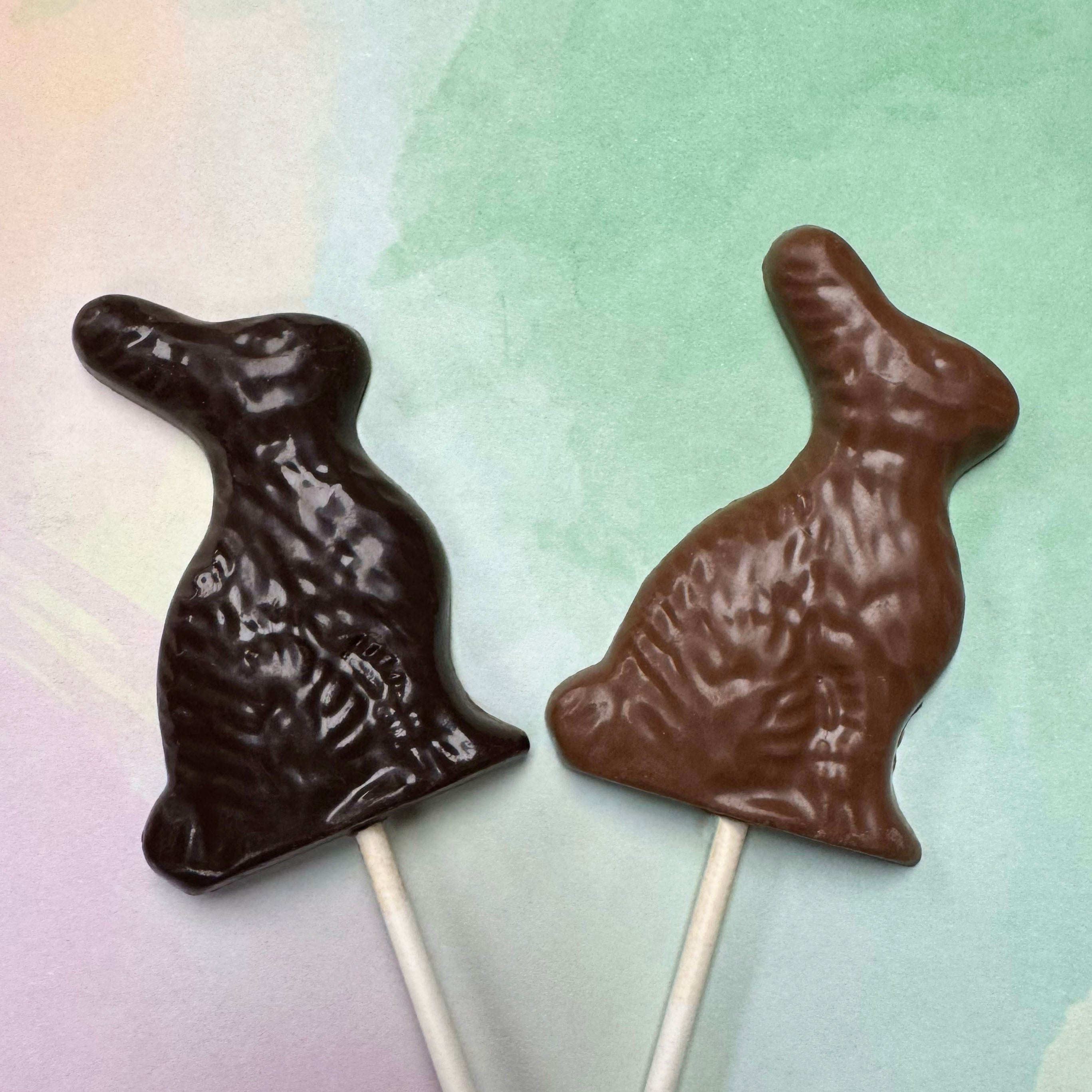 Two chocolate easter bunny lollipops on a pastel gradient background