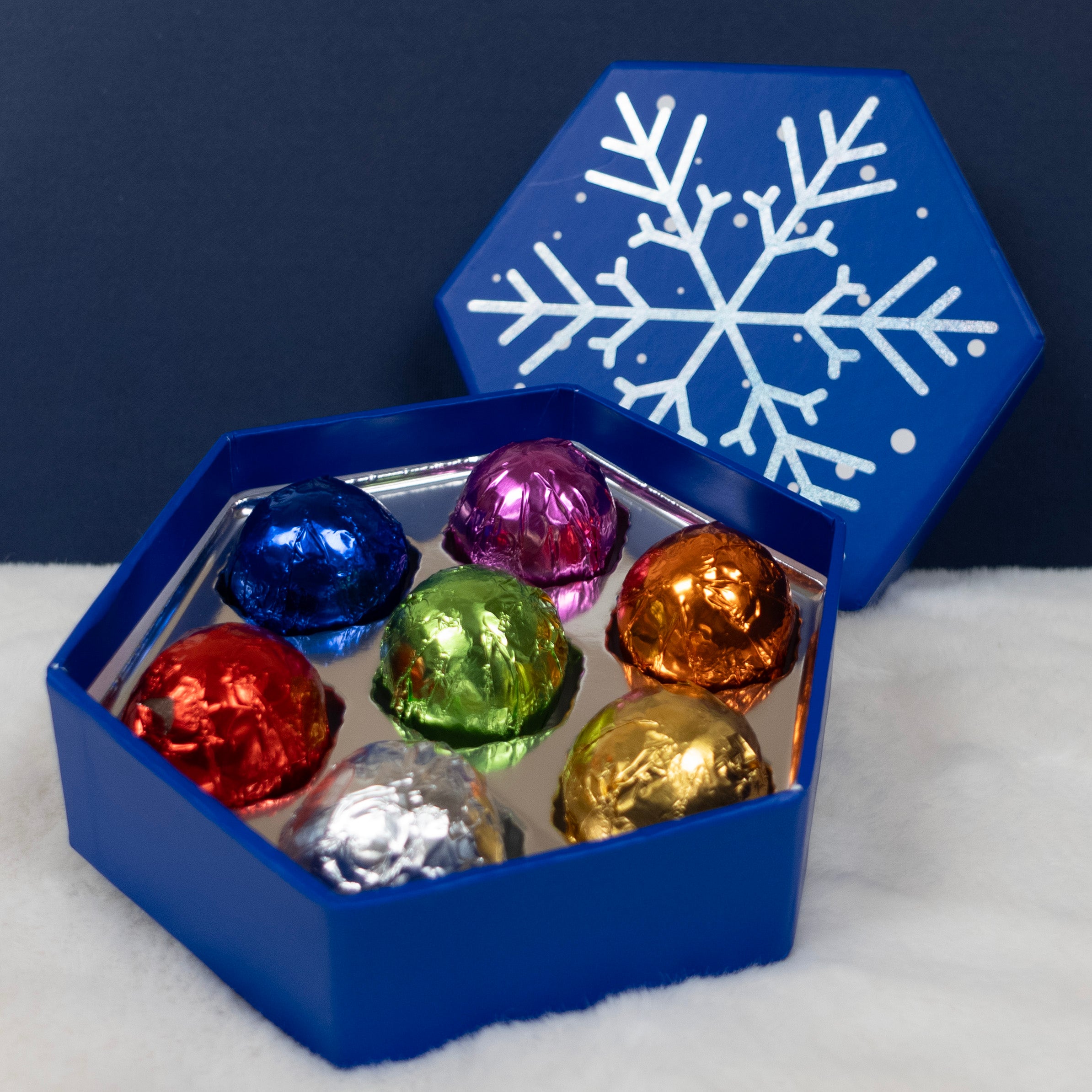 Blue hexagonal box with colorful foil-wrapped truffles and a snowflake design on a dark blue background.