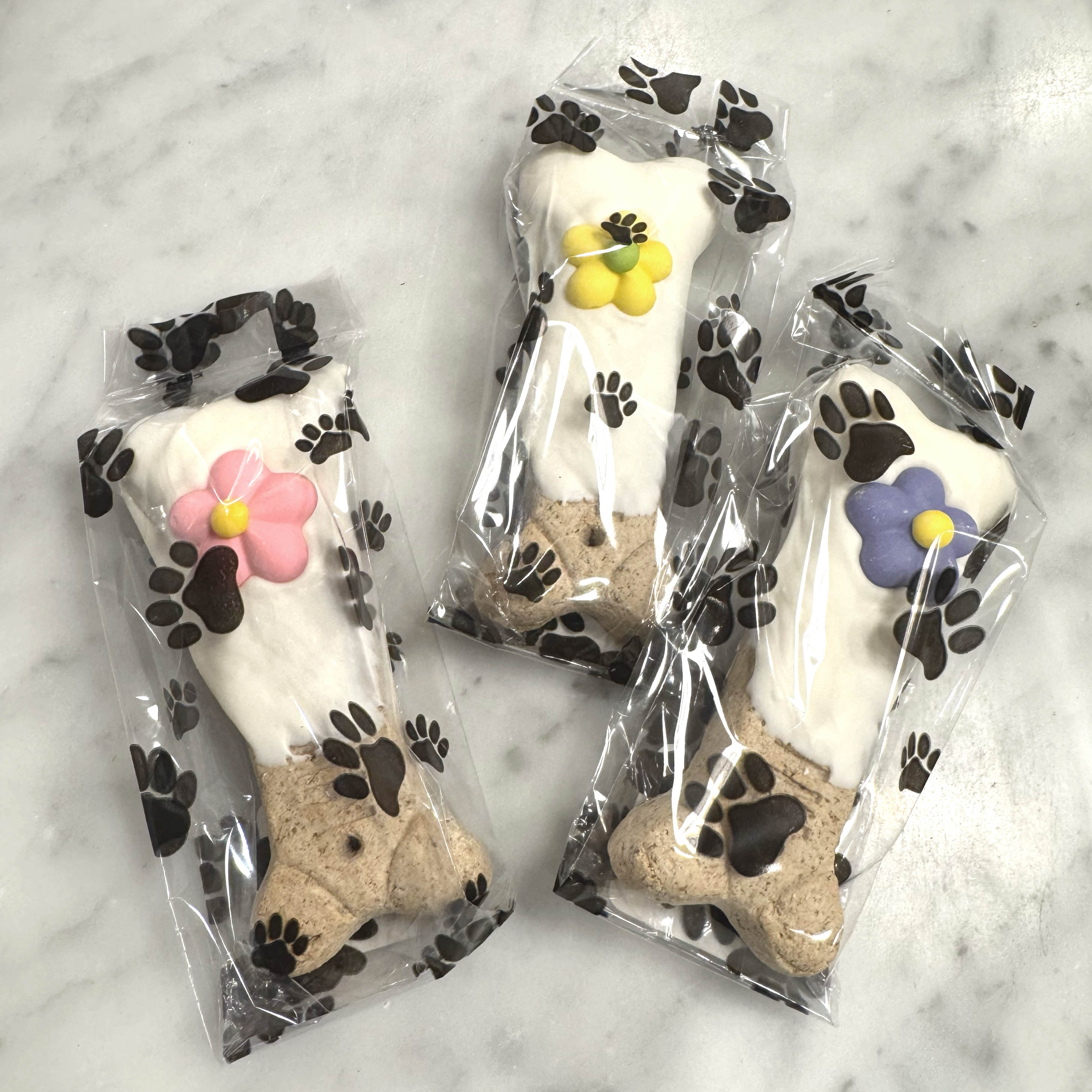 Three dog treats in clear packaging with decorative flowers on a marble surface