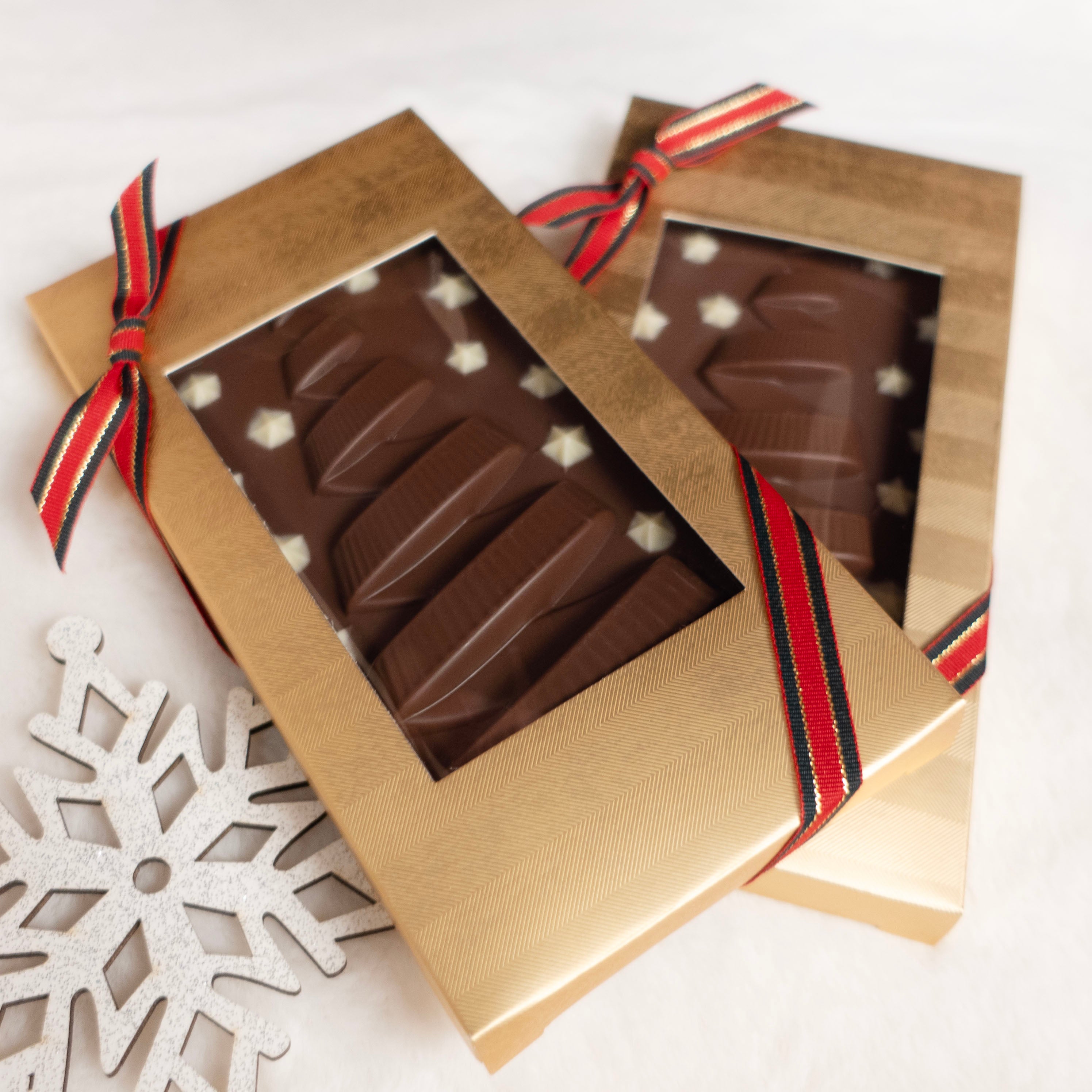 Chocolate bars with ribbon christmas trees in a gold box with a ribbon on a white background