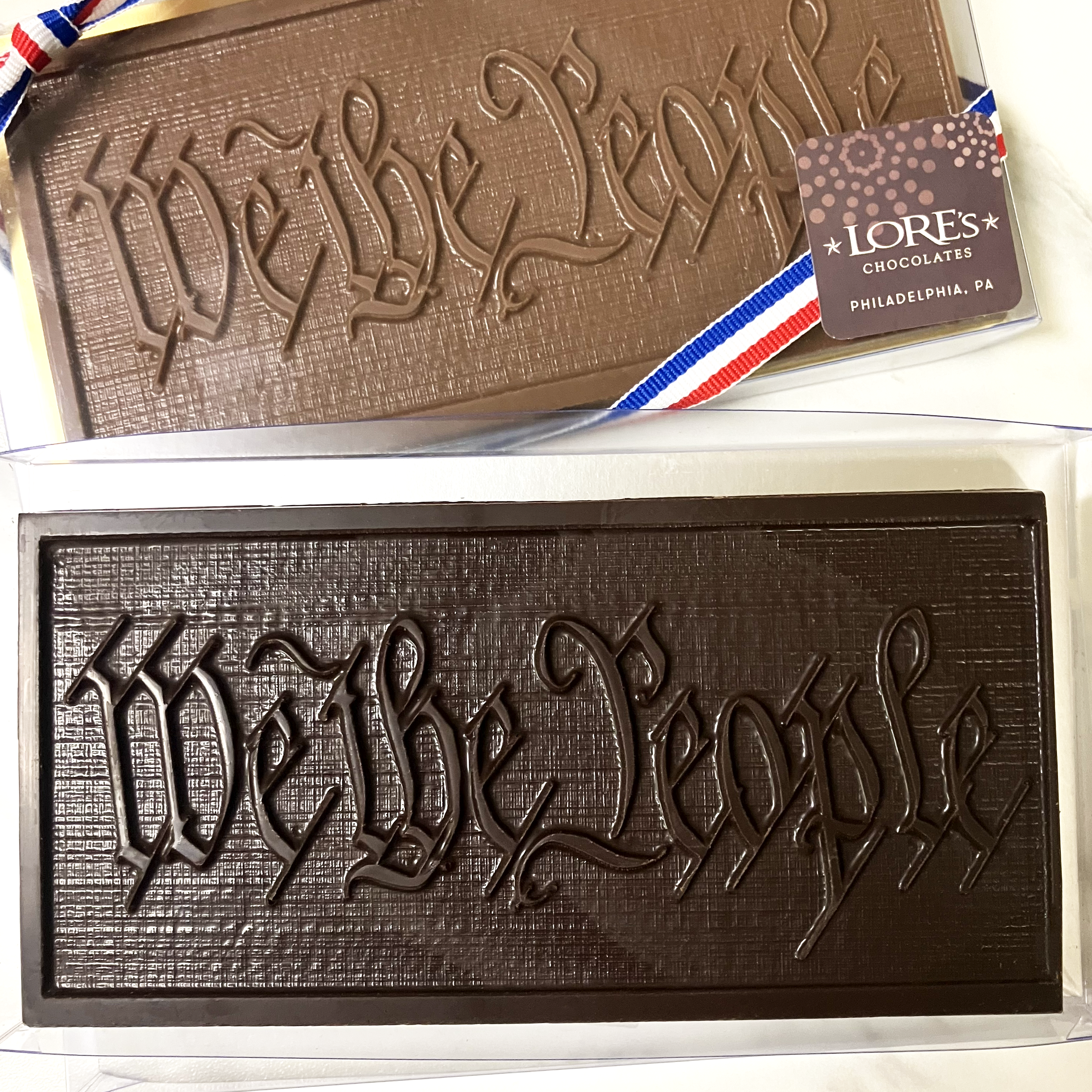 Handmade chocolate bars with 'We The People' text molded into the surface, packaged with a ribbon and tag indicating the brand and origin.