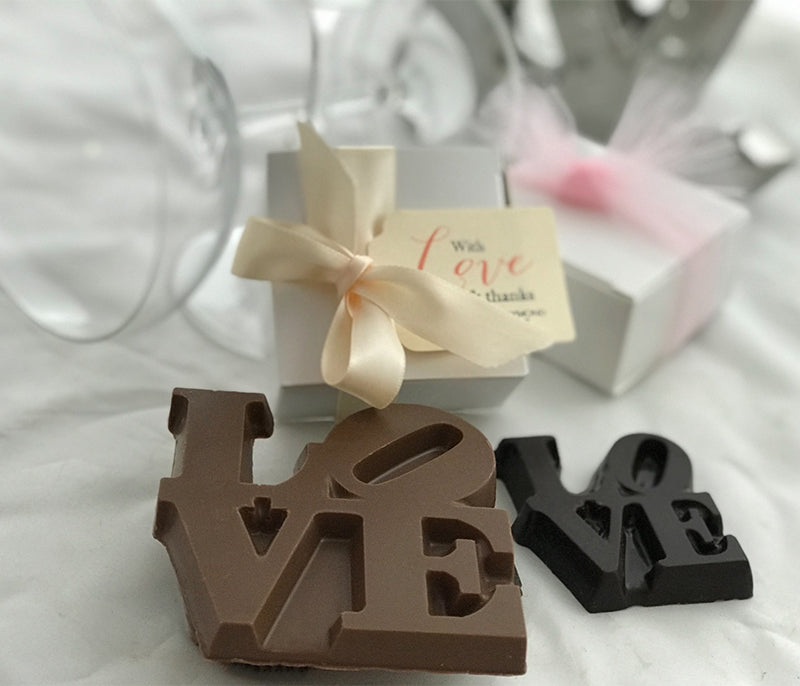 LOVE Chocolates from Lore's as wedding favors, with drinking glasses and white boxes of chocolate in the background.
