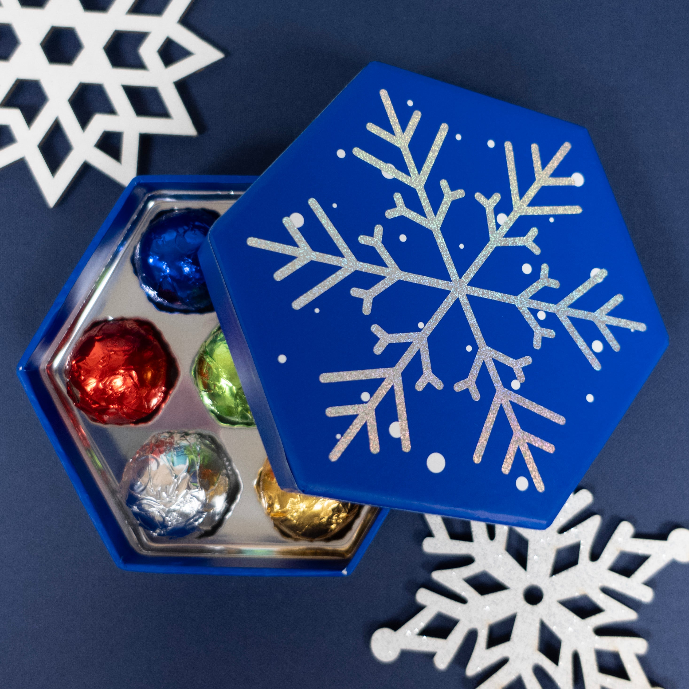 Blue hexagonal box with a snowflake design, containing wrapped chocolate truffles on a dark blue background with white snowflakes.