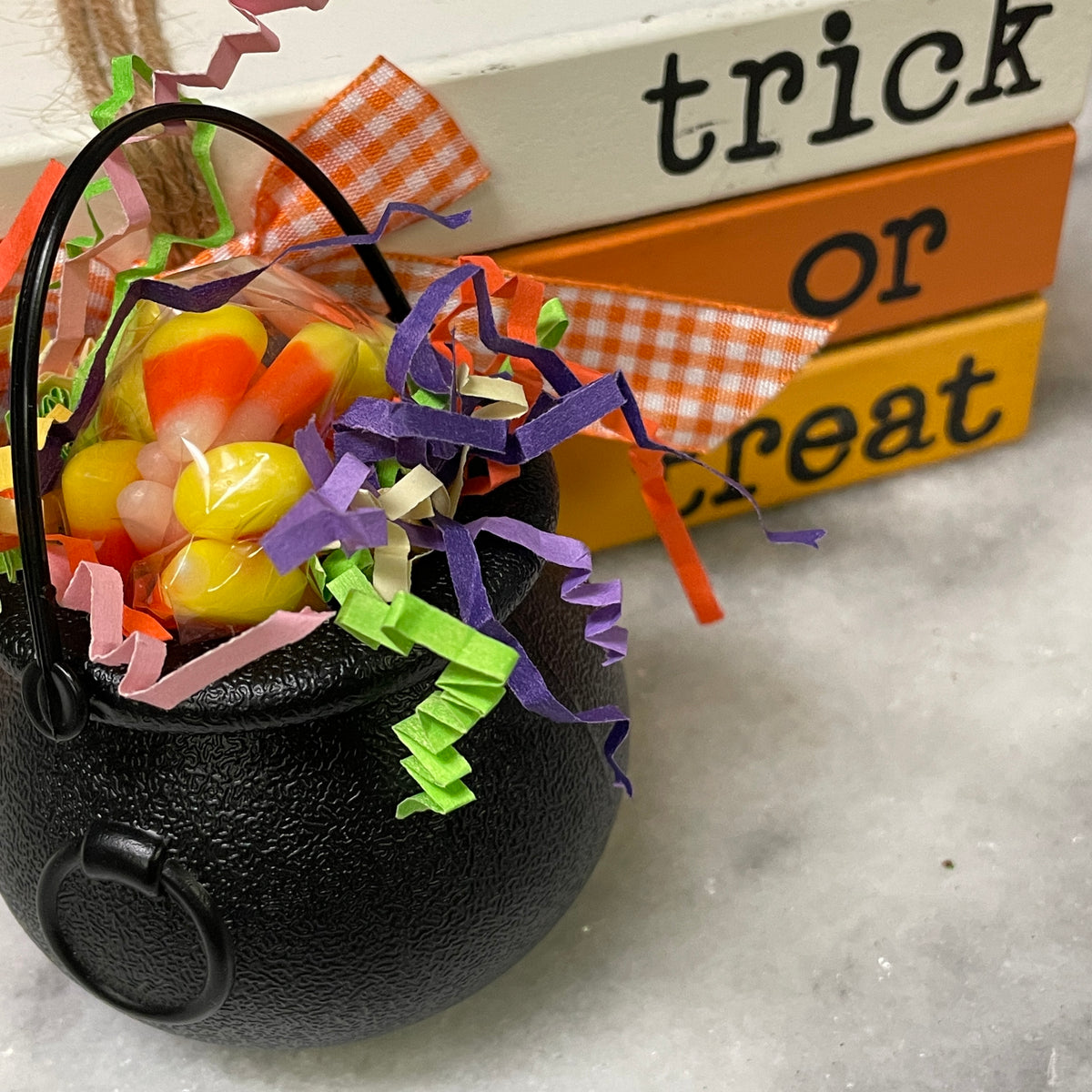 Black plastic cauldron with Halloween colored crinkled paper and a bag of candy corn
