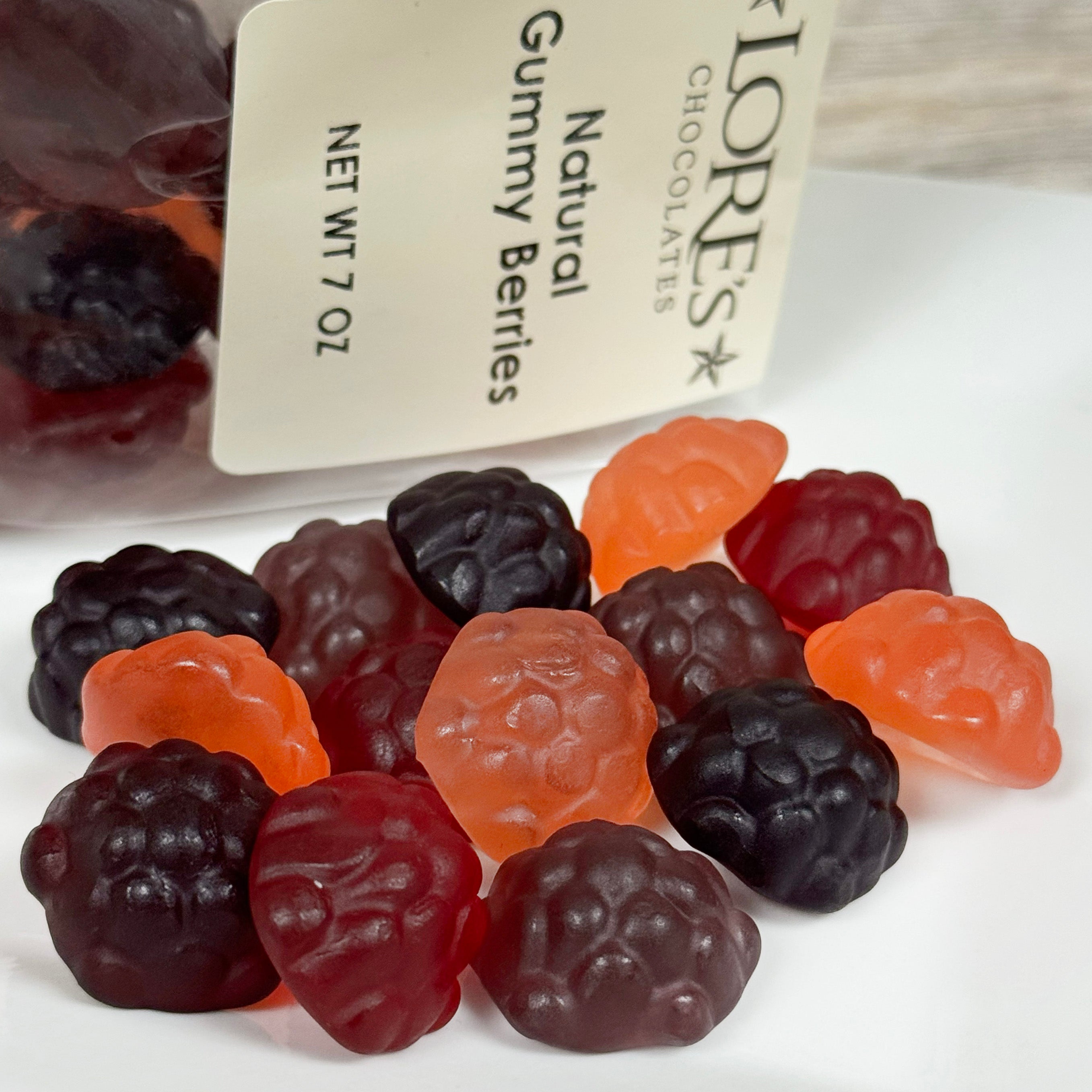 Gummy berries in black, red, and orange with a package labeled 'Lore's Chocolates' in the background.
