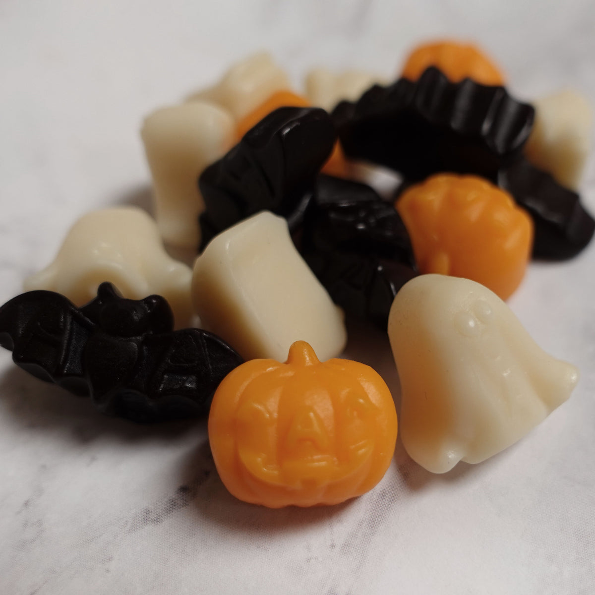 Halloween-themed gummy candies in black, orange, and white on a marble surface.