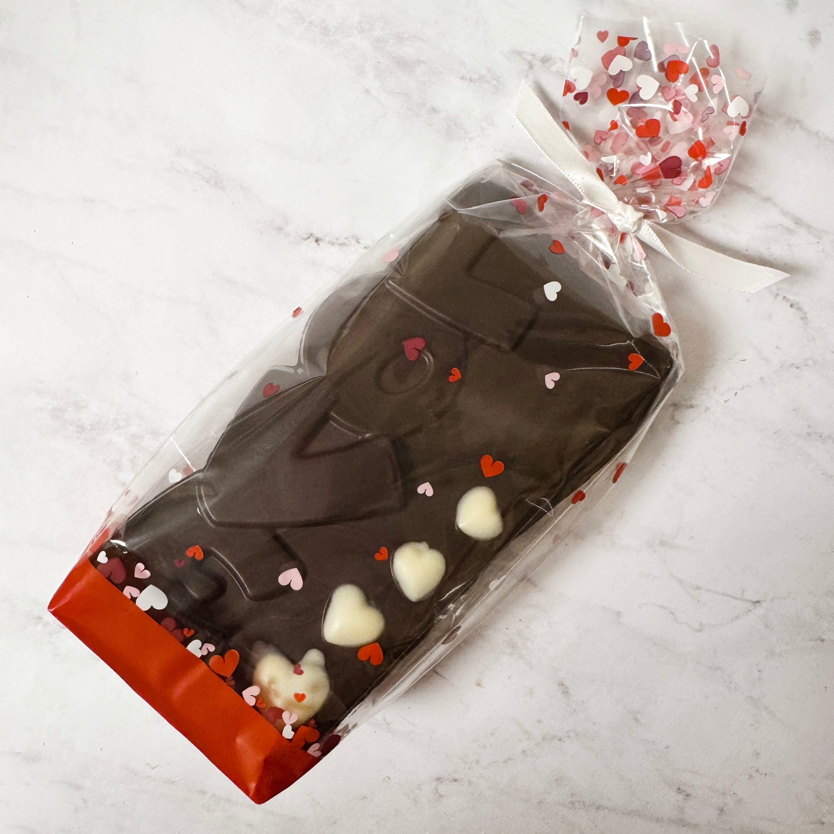 Chocolate bar with LOVE and white chocoalte hearts in clear packaging with  and red heart accents on a marble surface. made by  Lore's Chocolates in Philadelphia