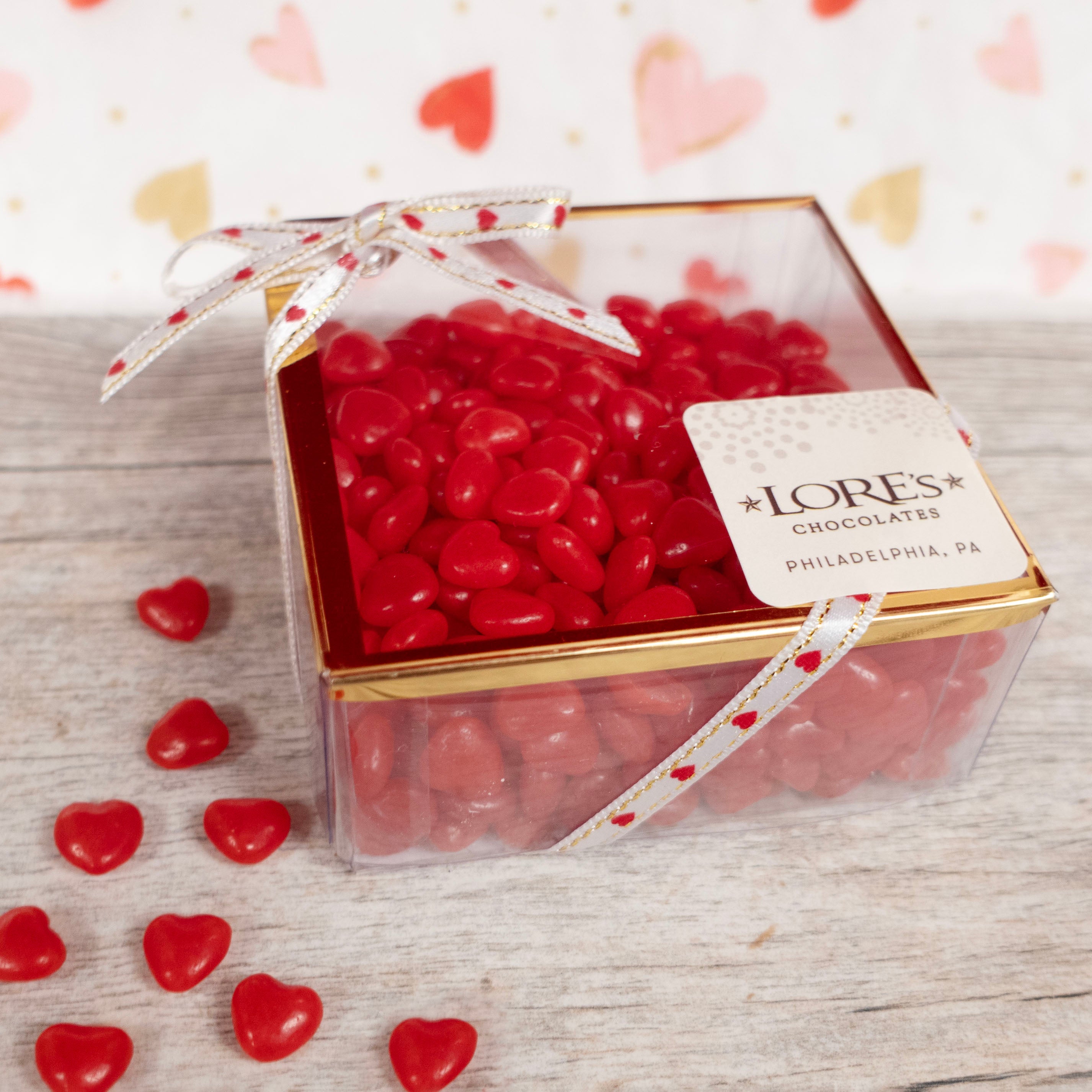 Box of red heart-shaped candies with a visible brand "Lore's Chocolates Philadelphia" label on a wooden surface.