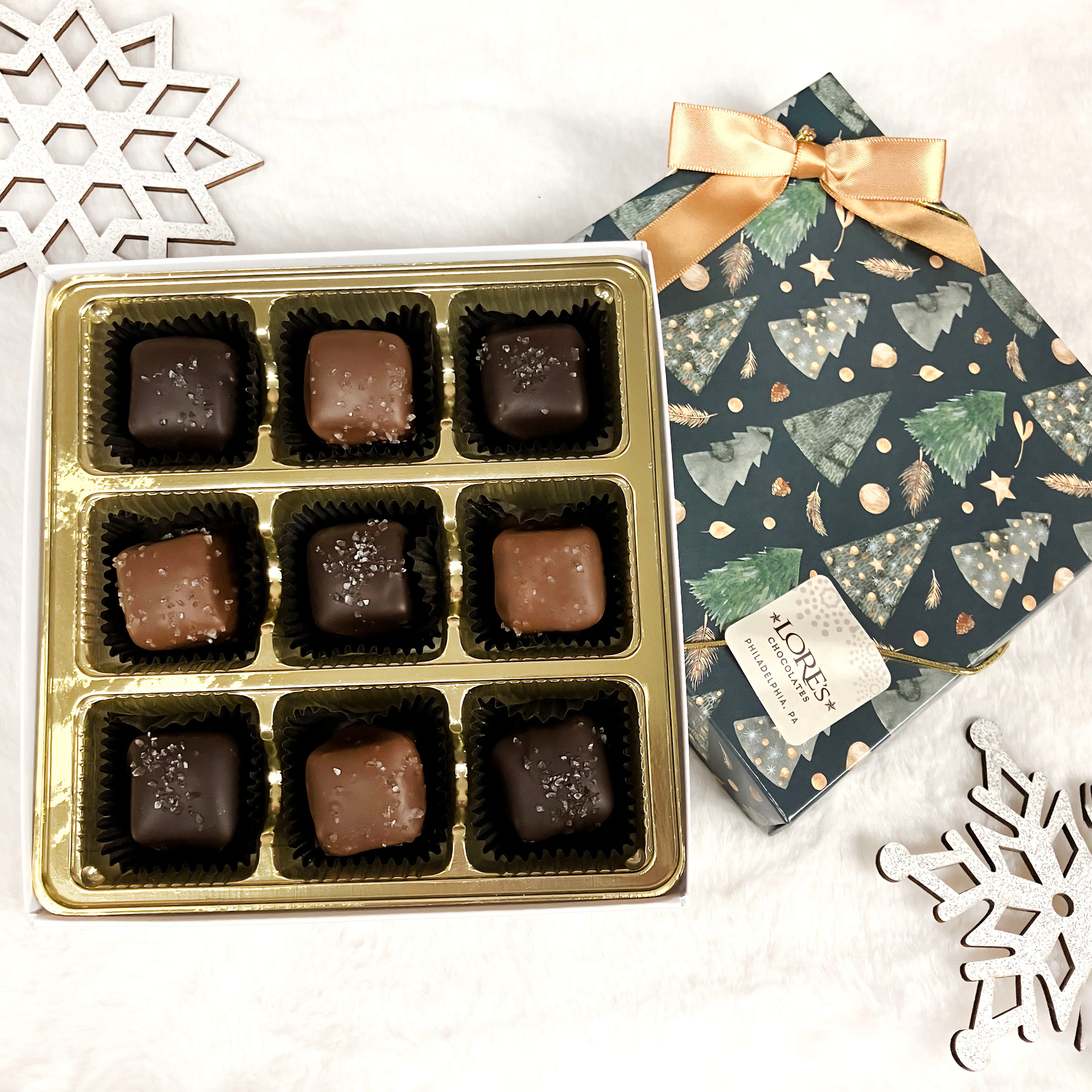 Box of lore's chocolates in a decorative Christmas-themed box on a white surface.