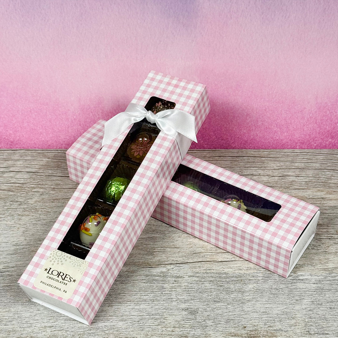 Chocolate truffles in a pink gingham box with a white ribbon on a wooden surface.