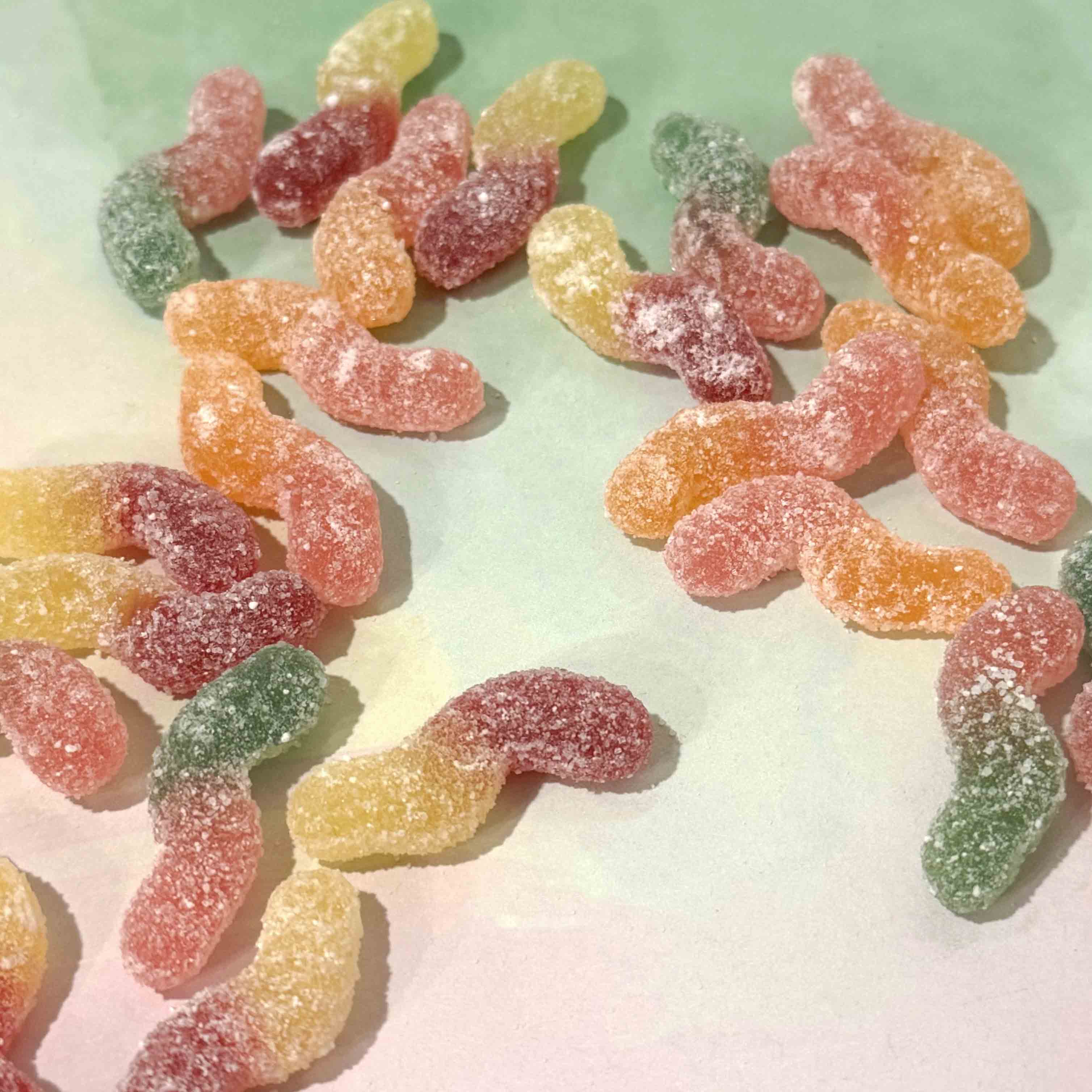 Colorful gummy worms on a light green and white gradient background