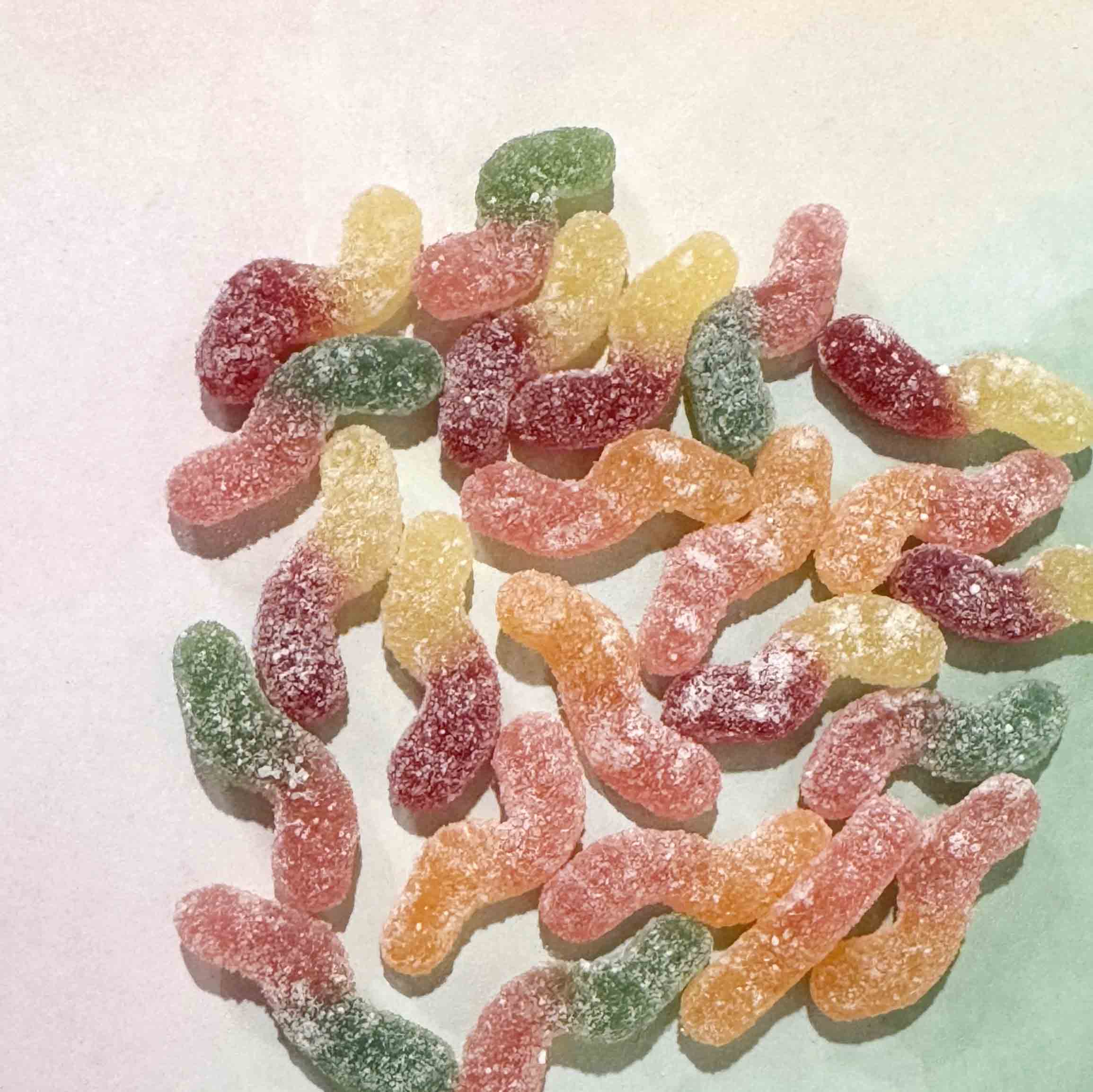 Colorful tiny sour gummy worms on a light background