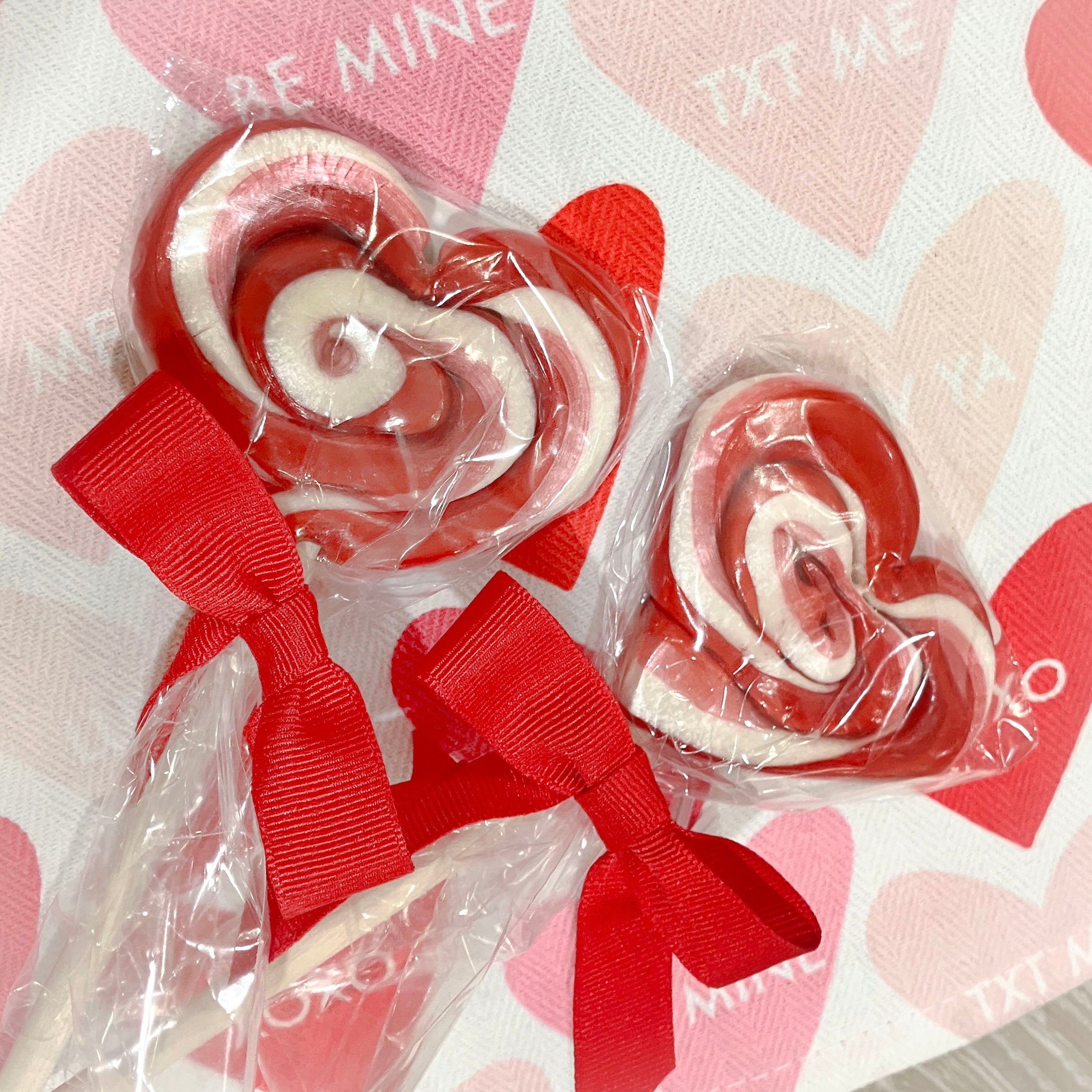 Heart-shaped lollipops with red ribbons on a heart-patterned background