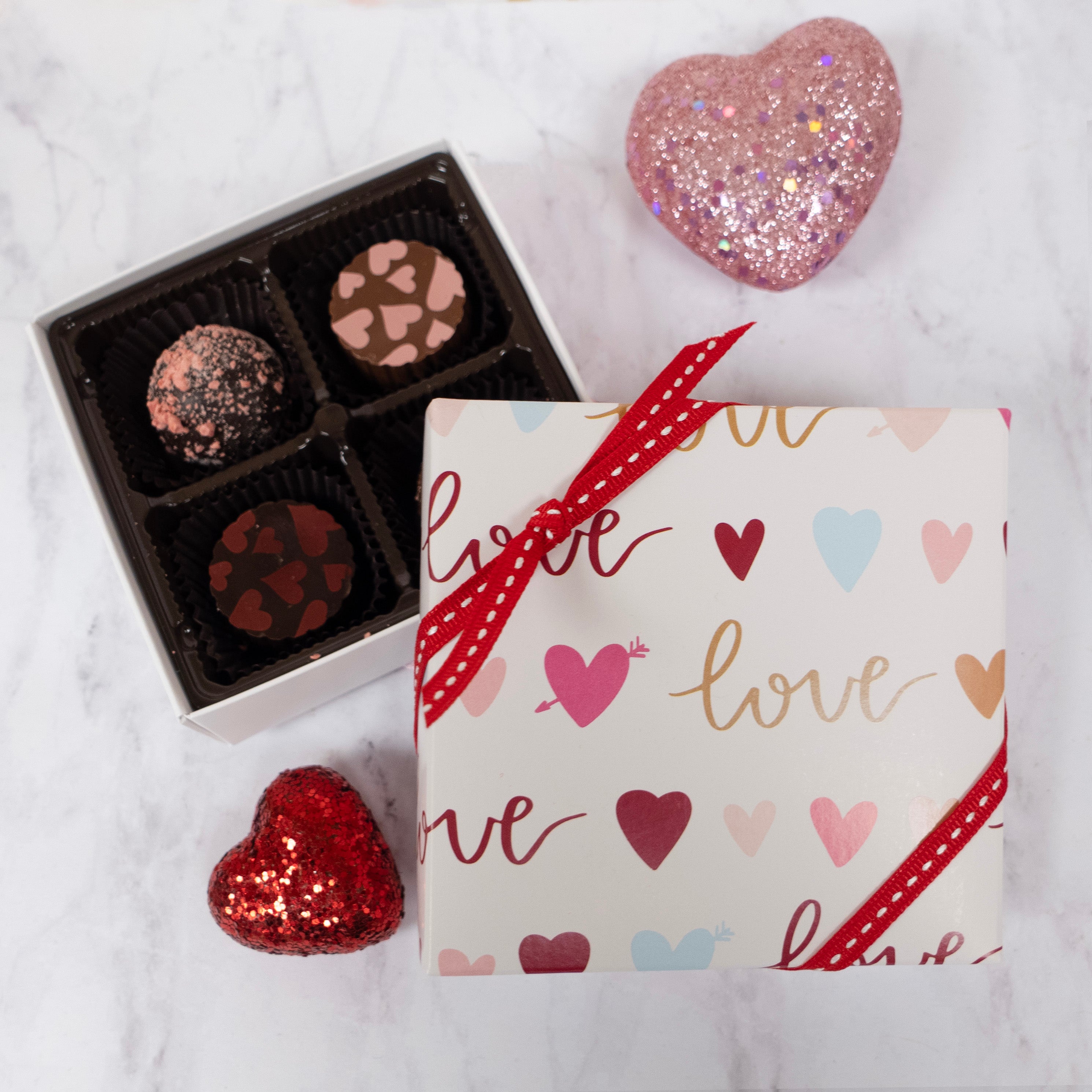 Box of truffle chocolates with hearts and the word 'love' on a marble surface.