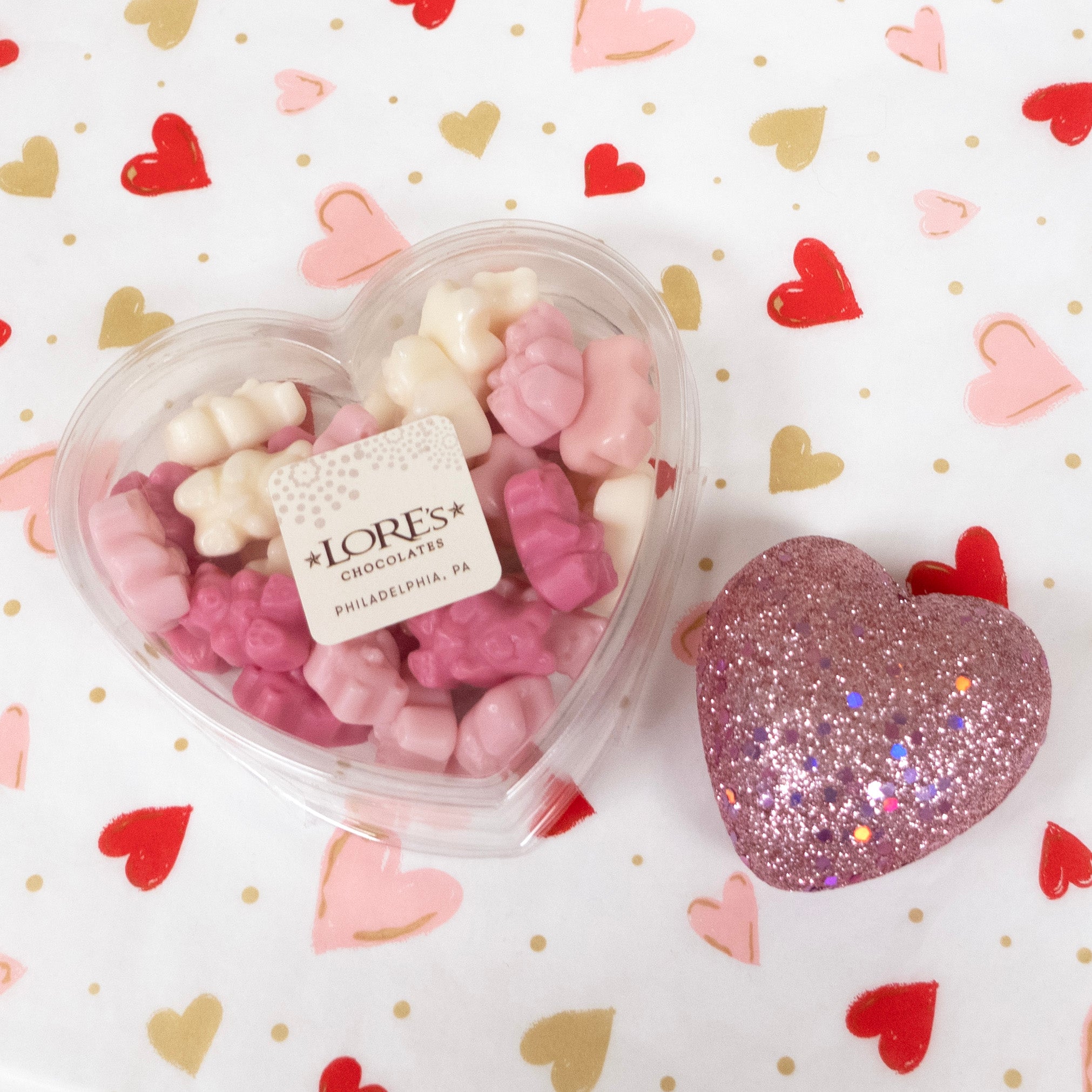 Heart-shaped container of gummy bears with a glittery heart on a heart-patterned background