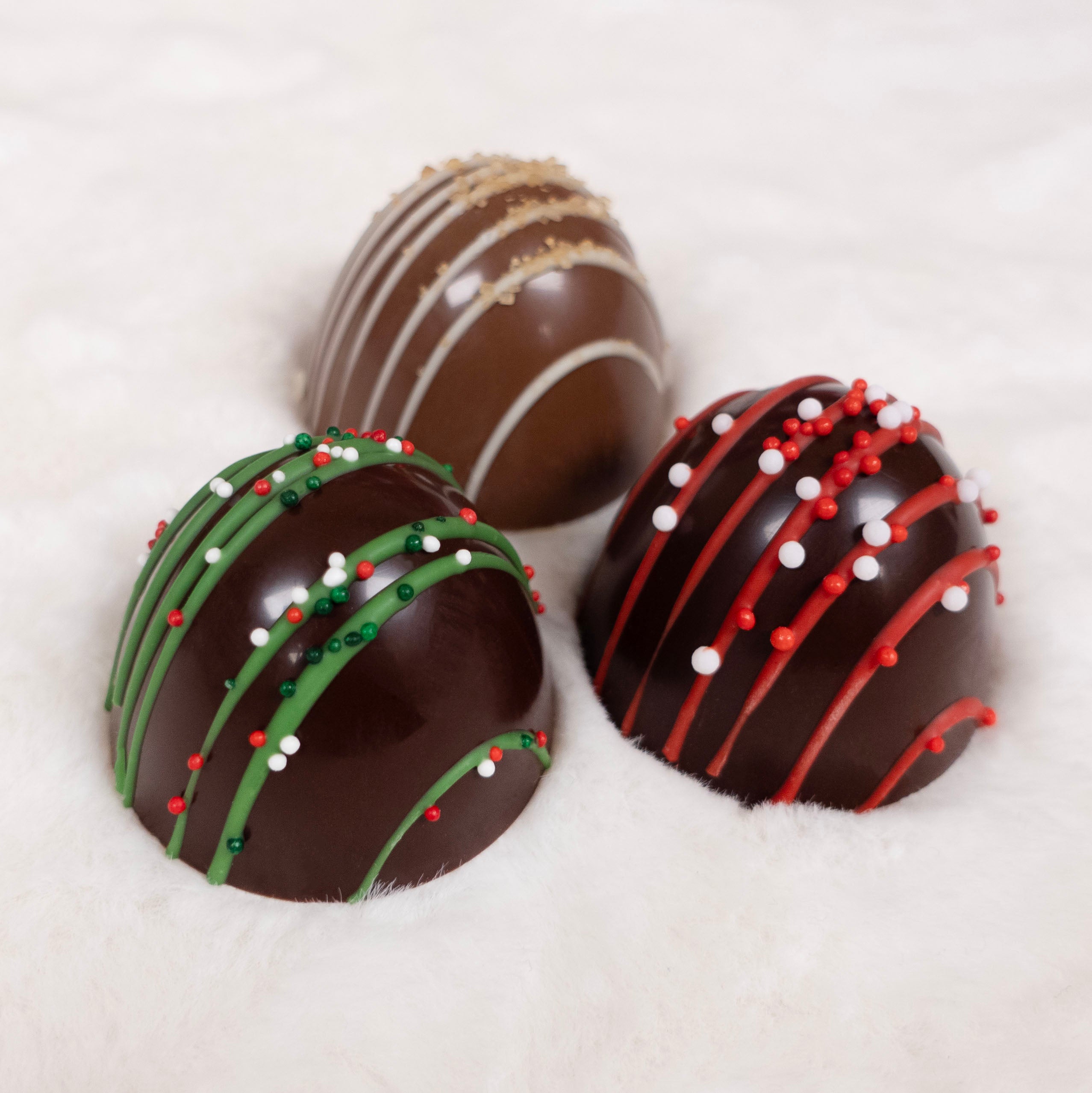 Three chocolate truffle domes with decorative drizzle and sprinkles on a white background