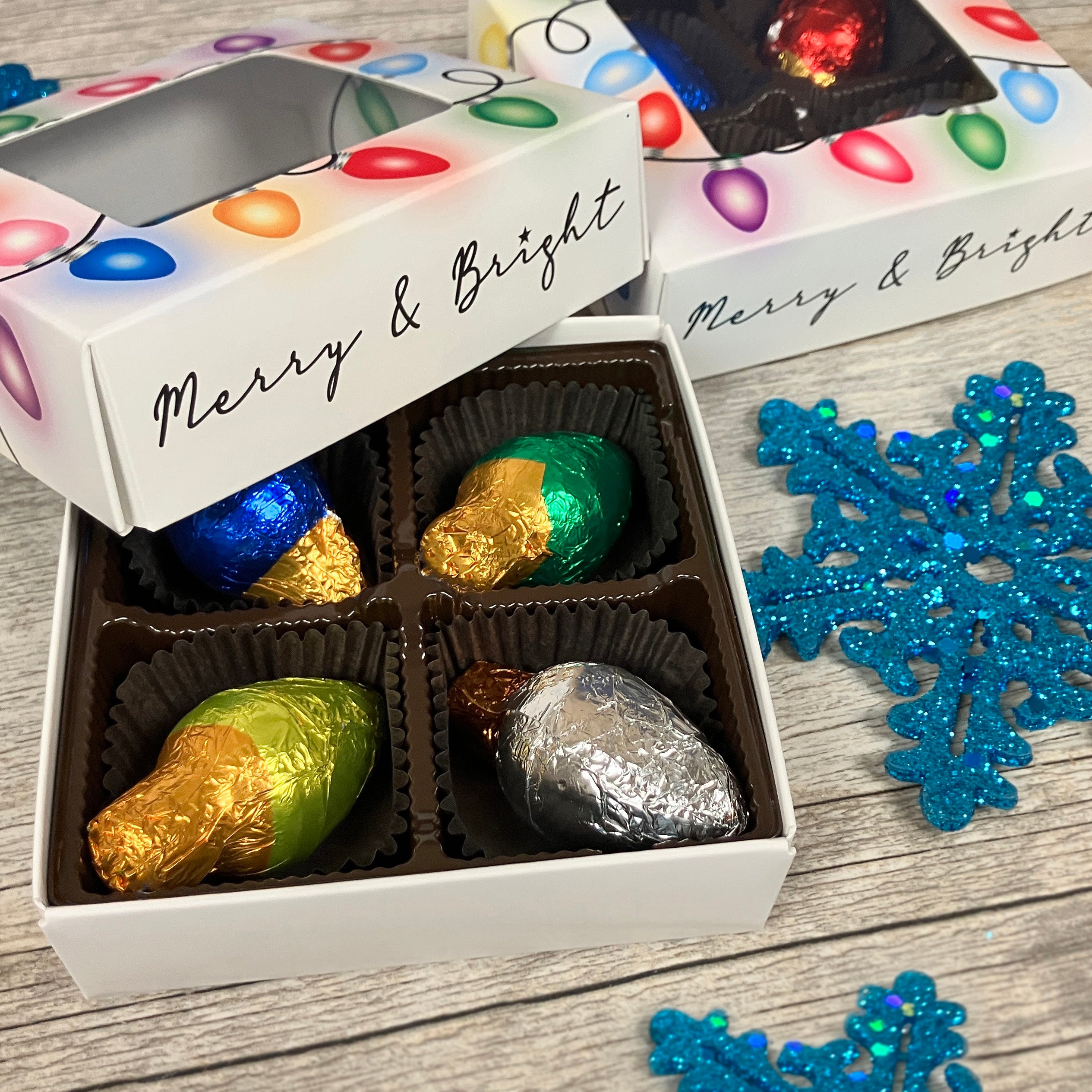 Box of chocolates with festive wrapping on a wooden surface with decorative snowflakes.