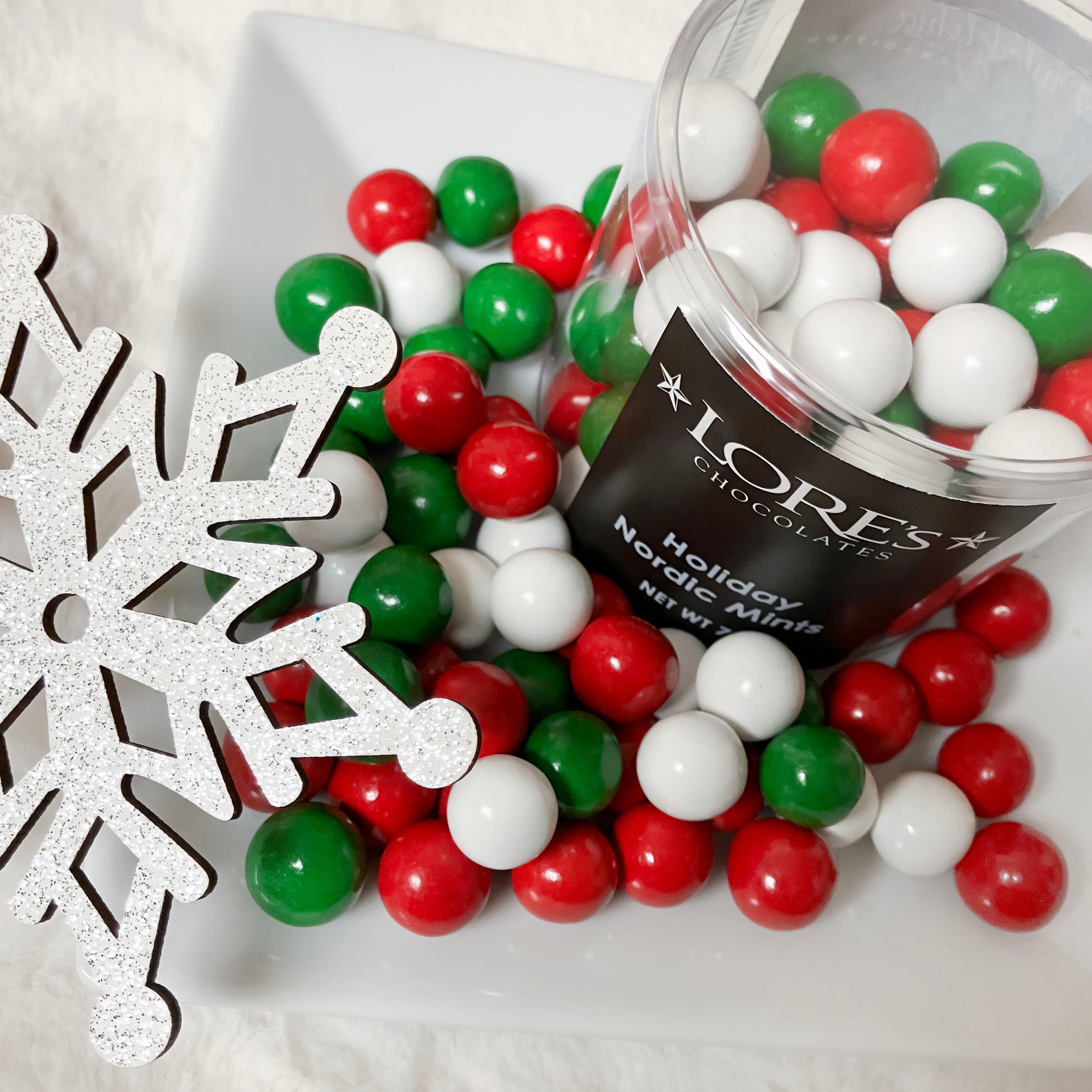 Container of Lore's Chocolates Holiday Nordic Mints with red, green, and white mints spilling out.