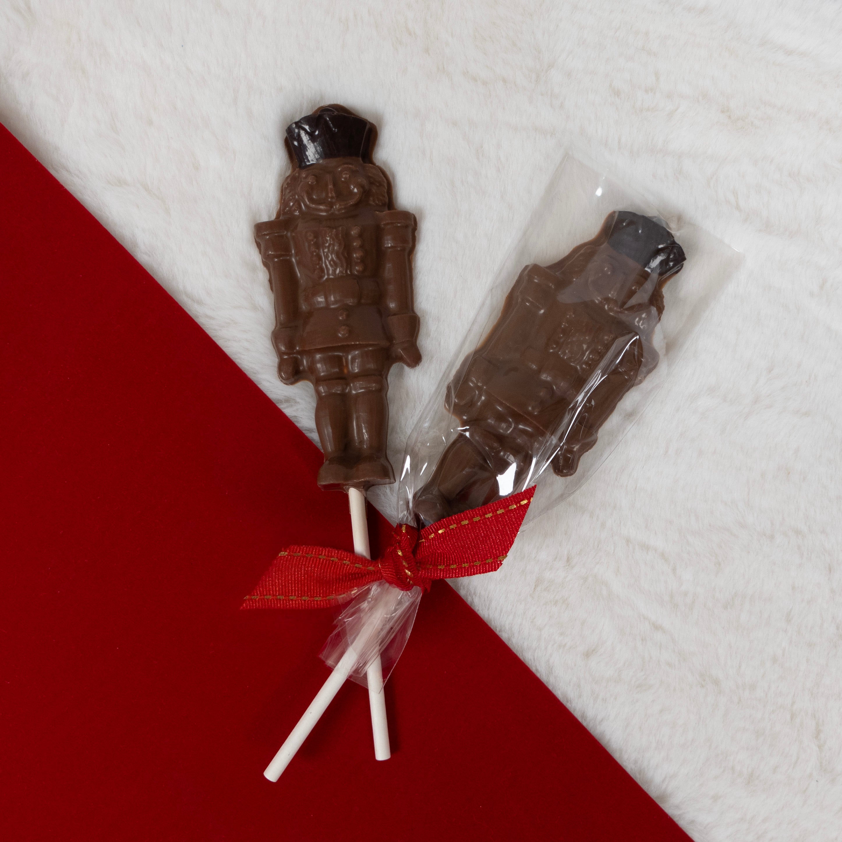 Chocolate soldier nutcracker lollipops with a red ribbon on a white and red background