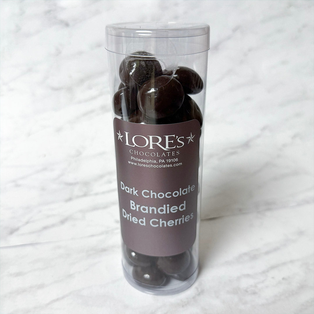 Clear cylindrical container of dark chocolate brandied dried cherries with a label on a white textured background